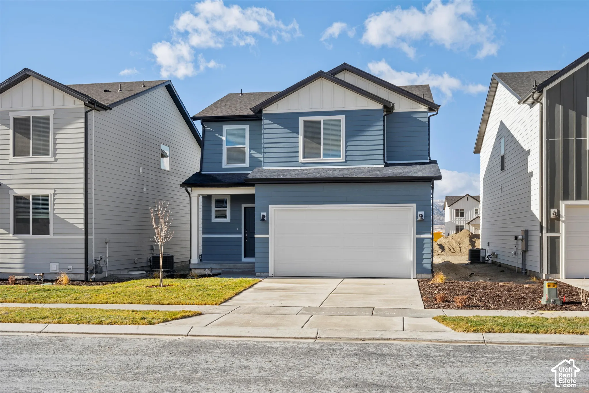 *DISCLAIMER* Elevation and exterior color may vary. Two-story residence featuring blue horizontal lap siding, white vertical board-and-batten gable accents, a concrete driveway, a two-car garage, and a covered front entryway