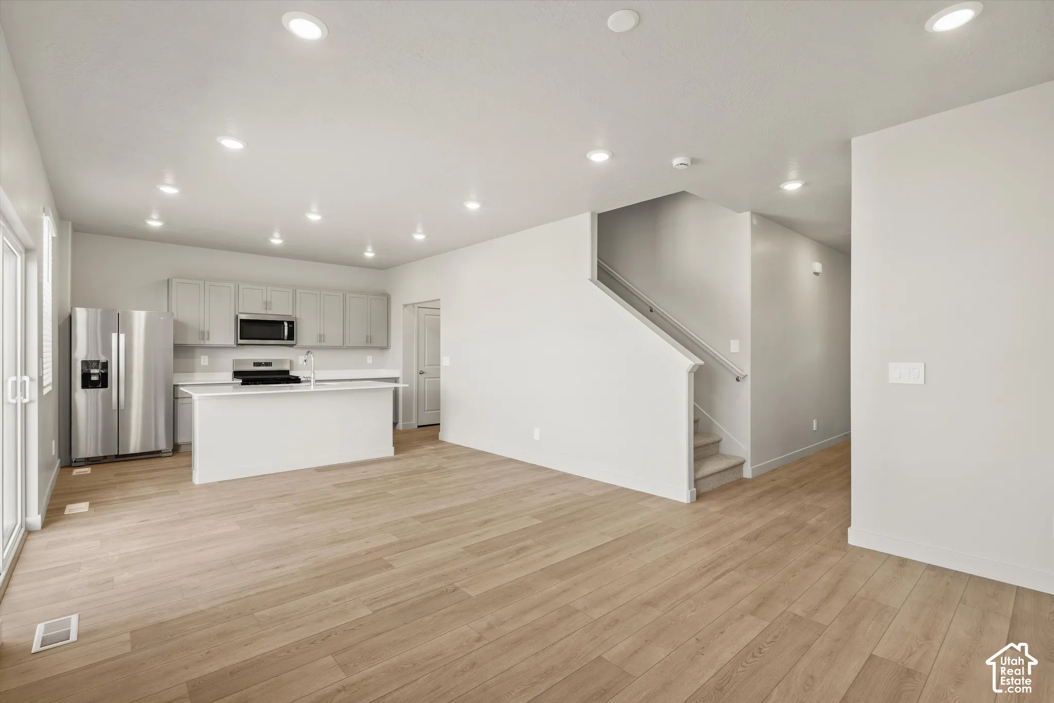 Open-concept interior featuring light wood-finish flooring, recessed lighting, a central kitchen island, stainless steel refrigerator, and built-in microwave