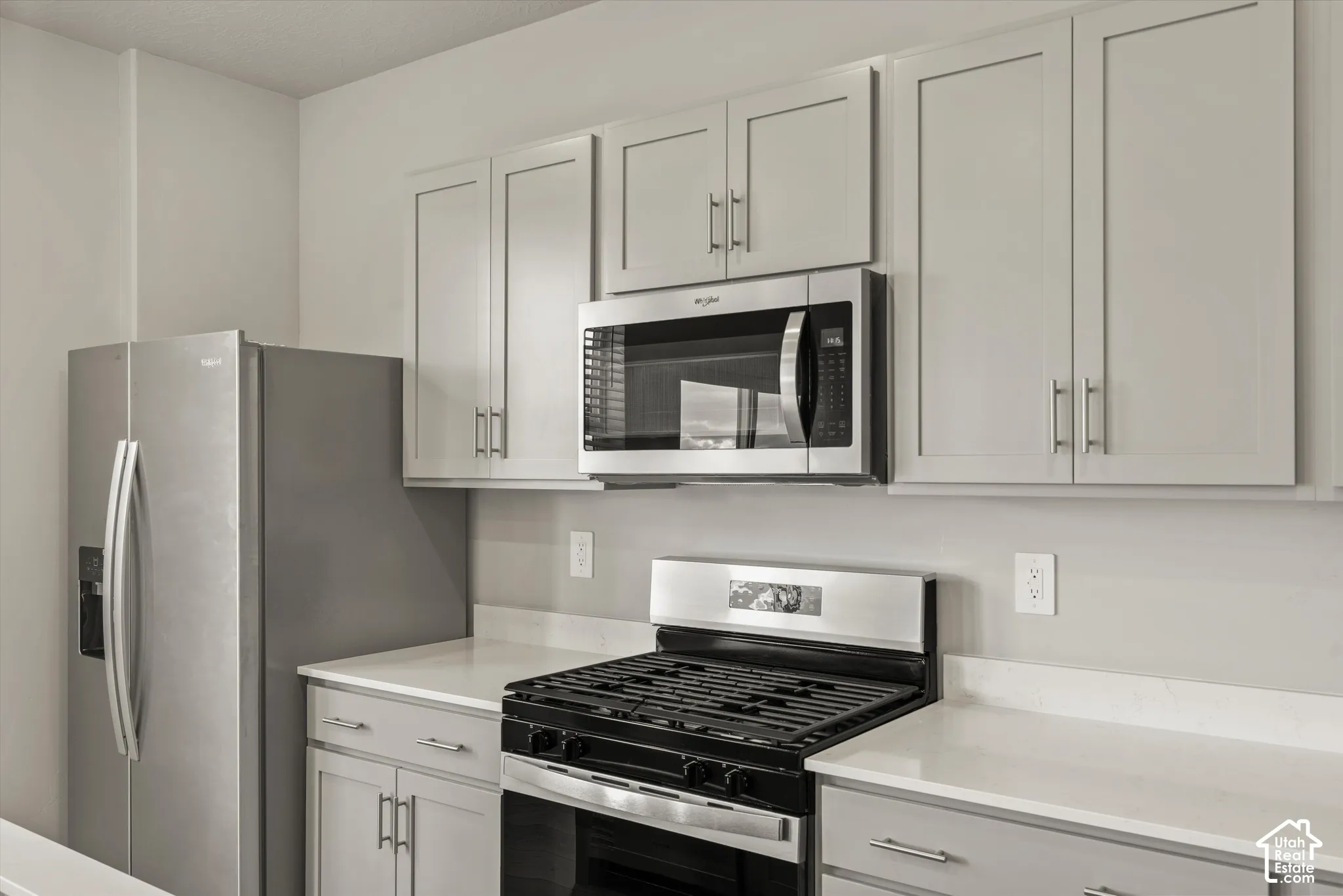 Kitchen featuring light gray shaker-style cabinetry, white solid-surface countertops, and stainless steel appliances including a side-by-side refrigerator, built-in microwave, and gas range