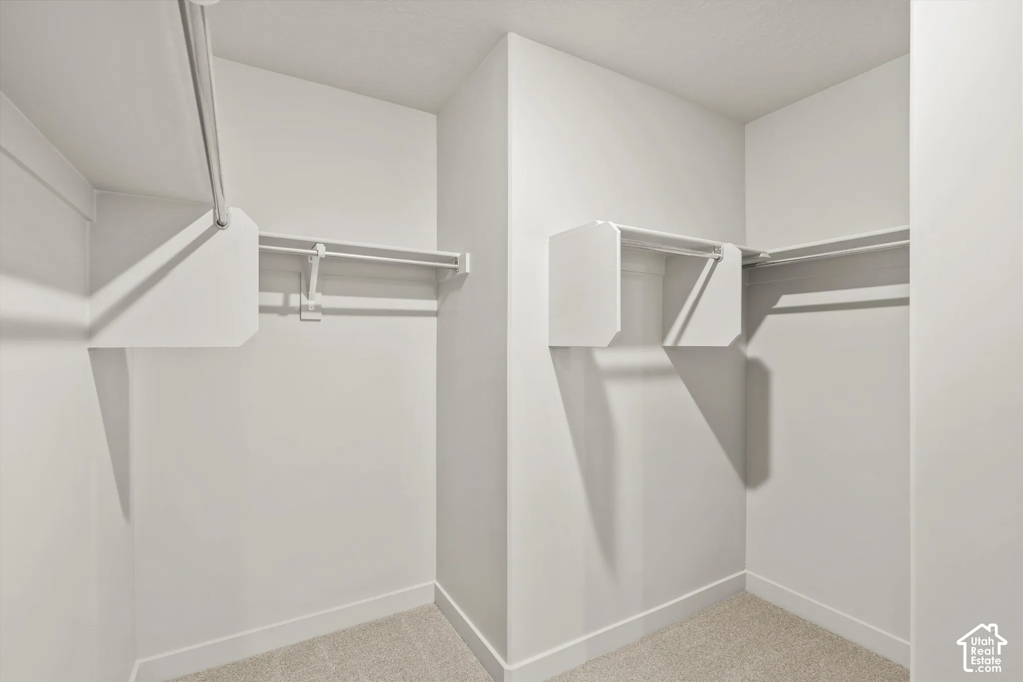 Walk-in closet featuring neutral carpet flooring and integrated white shelving with built-in metal garment rods
