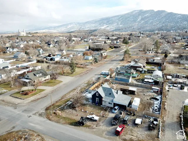 Aerial perspective featuring a detached residential structure, asphalt-shingle roof, wood-frame construction, perimeter fencing, and a mountainous backdrop