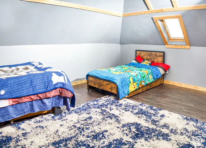 Vaulted ceiling featuring exposed wood beams, skylight with wood trim, and wood-finish flooring