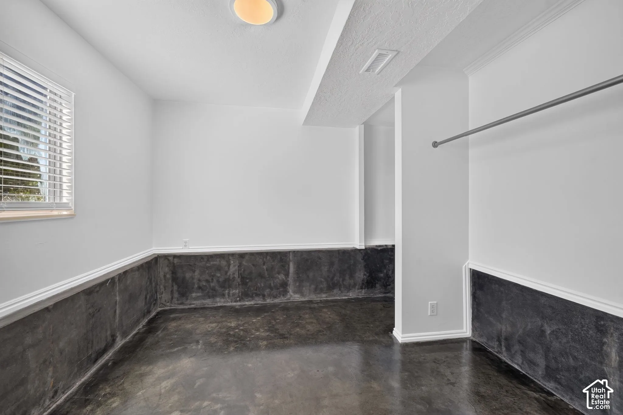 Interior space featuring polished concrete flooring, concrete lower-wall detailing, a ceiling-mounted light fixture, and a built-in metal clothing rod