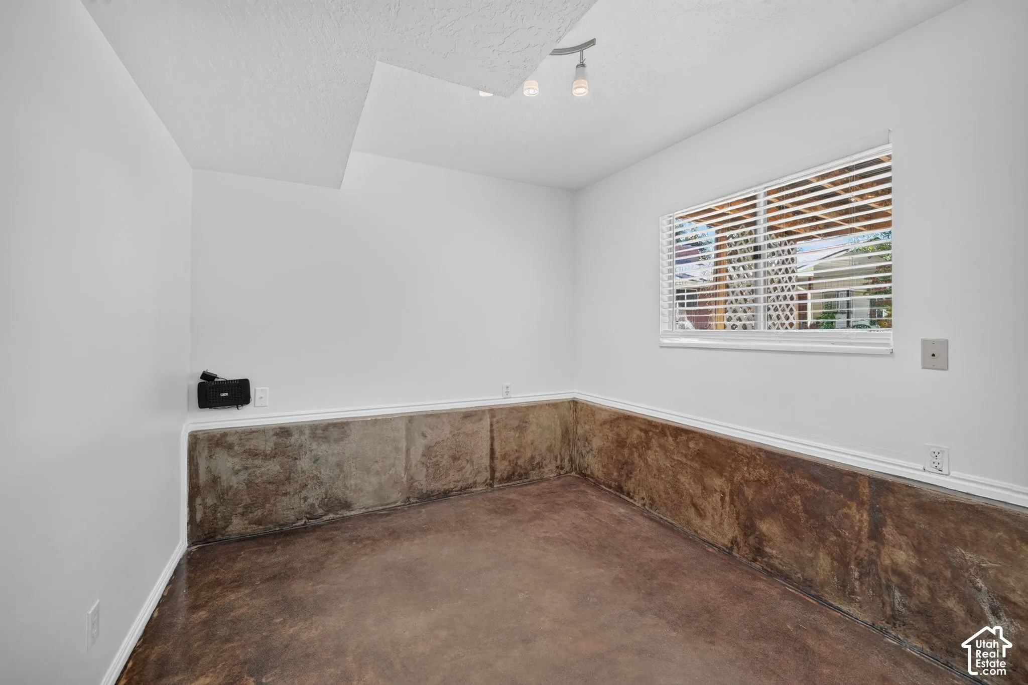 Room featuring exposed concrete lower walls, stained concrete flooring, white walls, horizontal window blinds, and overhead track lighting