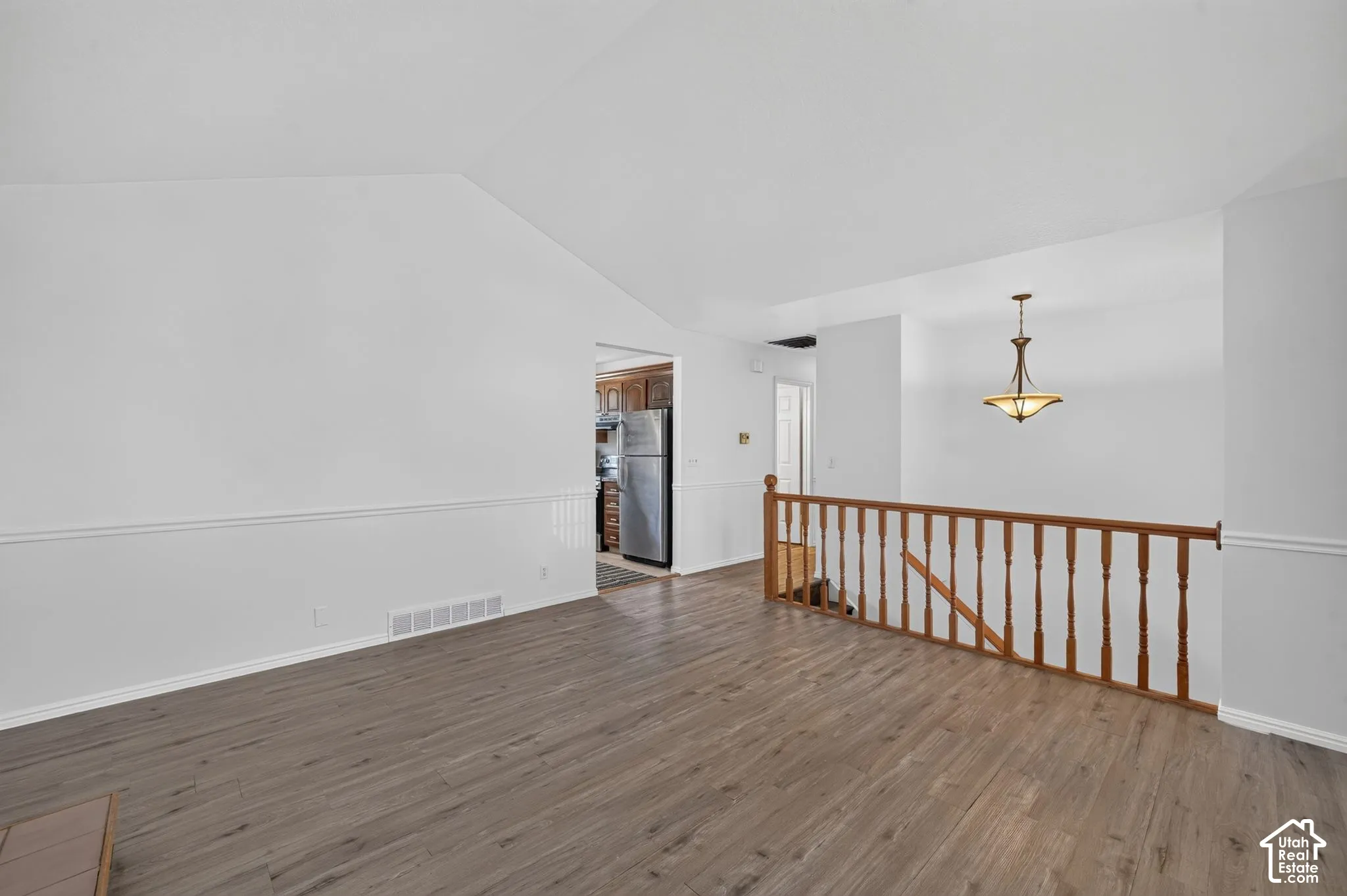 Vaulted ceilings, wood-finish flooring, wainscoting, stained wood railing, and an elevated pendant light fixture