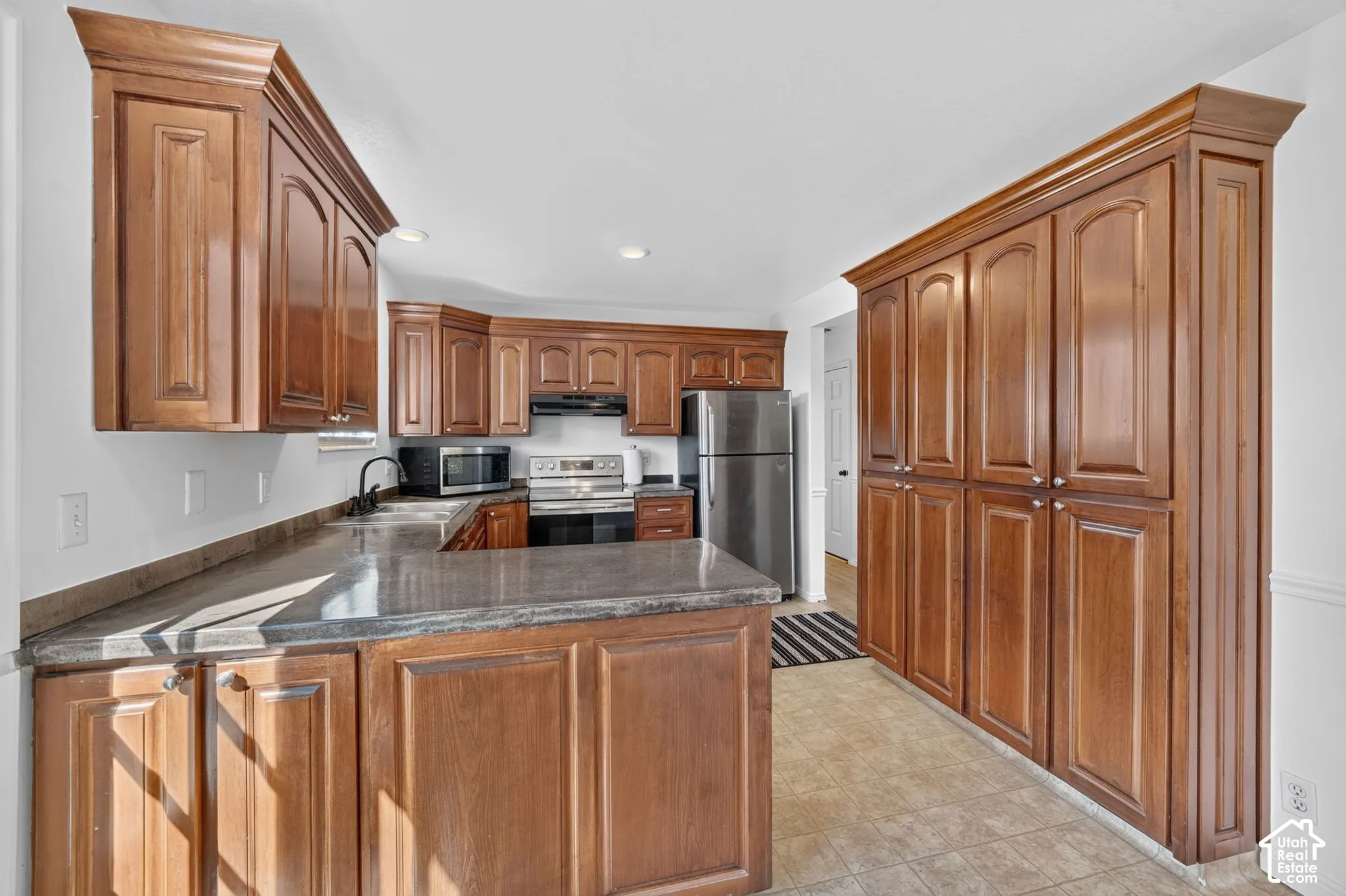 Kitchen featuring stained wood cabinetry, floor-to-ceiling storage, stone-finish countertops, stainless steel appliances, and recessed lighting