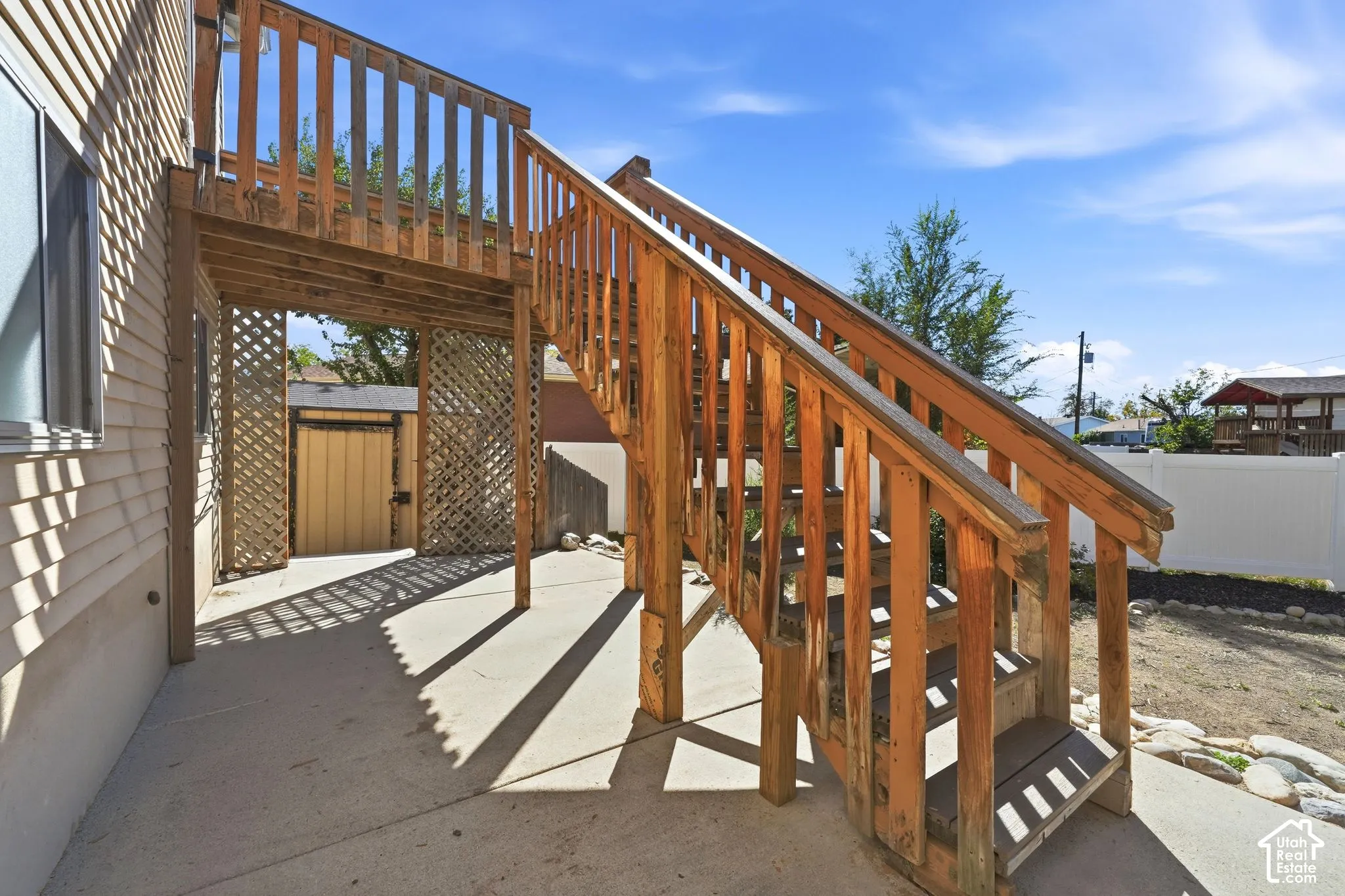 Concrete patio featuring a wood staircase with balustrades, wood lattice screening, and a fenced yard