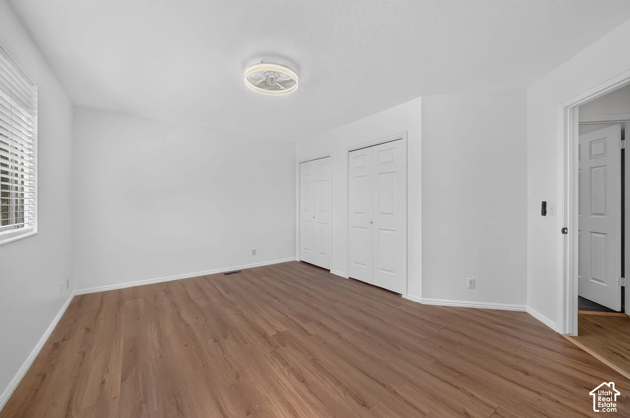 Interior room featuring wood-finish flooring, two sets of white paneled closet doors, a modern circular ceiling light fixture, and horizontal blind window treatments