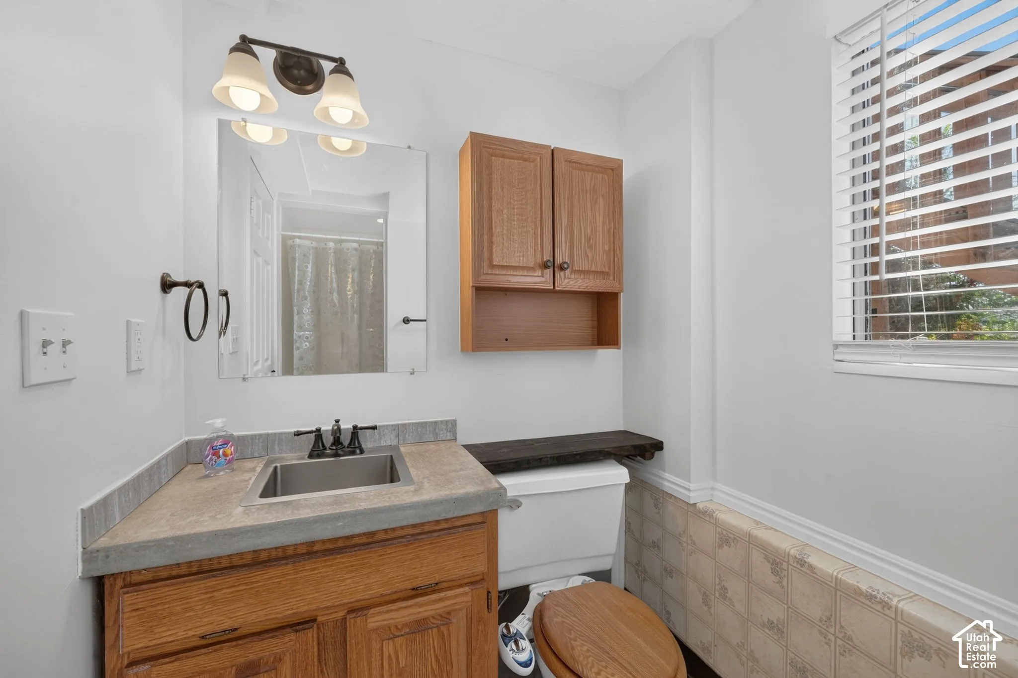 Bathroom featuring a wood-finish vanity with an integrated rectangular sink, matte-finish faucet, wall-mounted wood cabinetry, and window with horizontal blinds