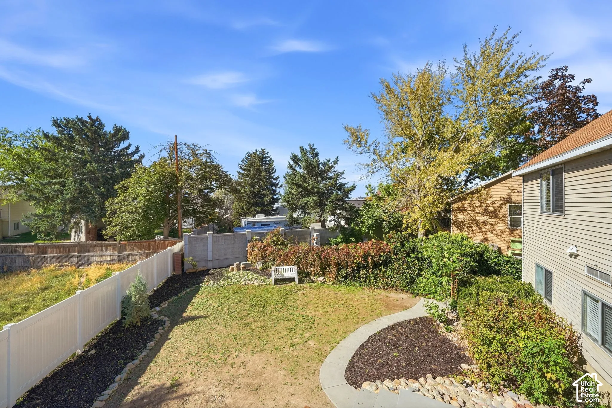 Backyard featuring a privacy fence, concrete walkway, stone landscaping accents, and mature trees