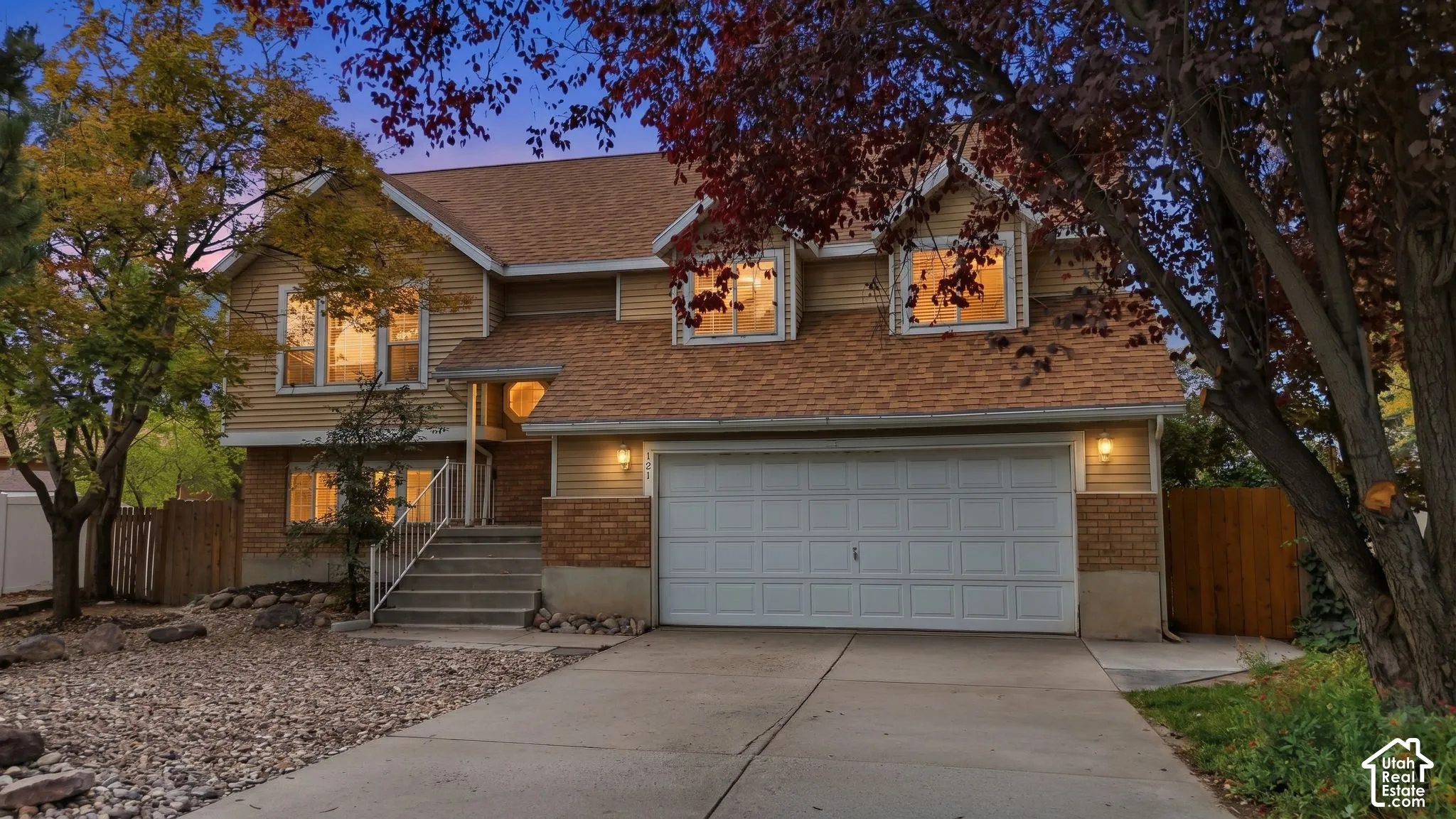 Two-story exterior featuring tan horizontal siding, brick masonry detailing, an attached two-car garage, steep roof pitches, and multiple dormer windows