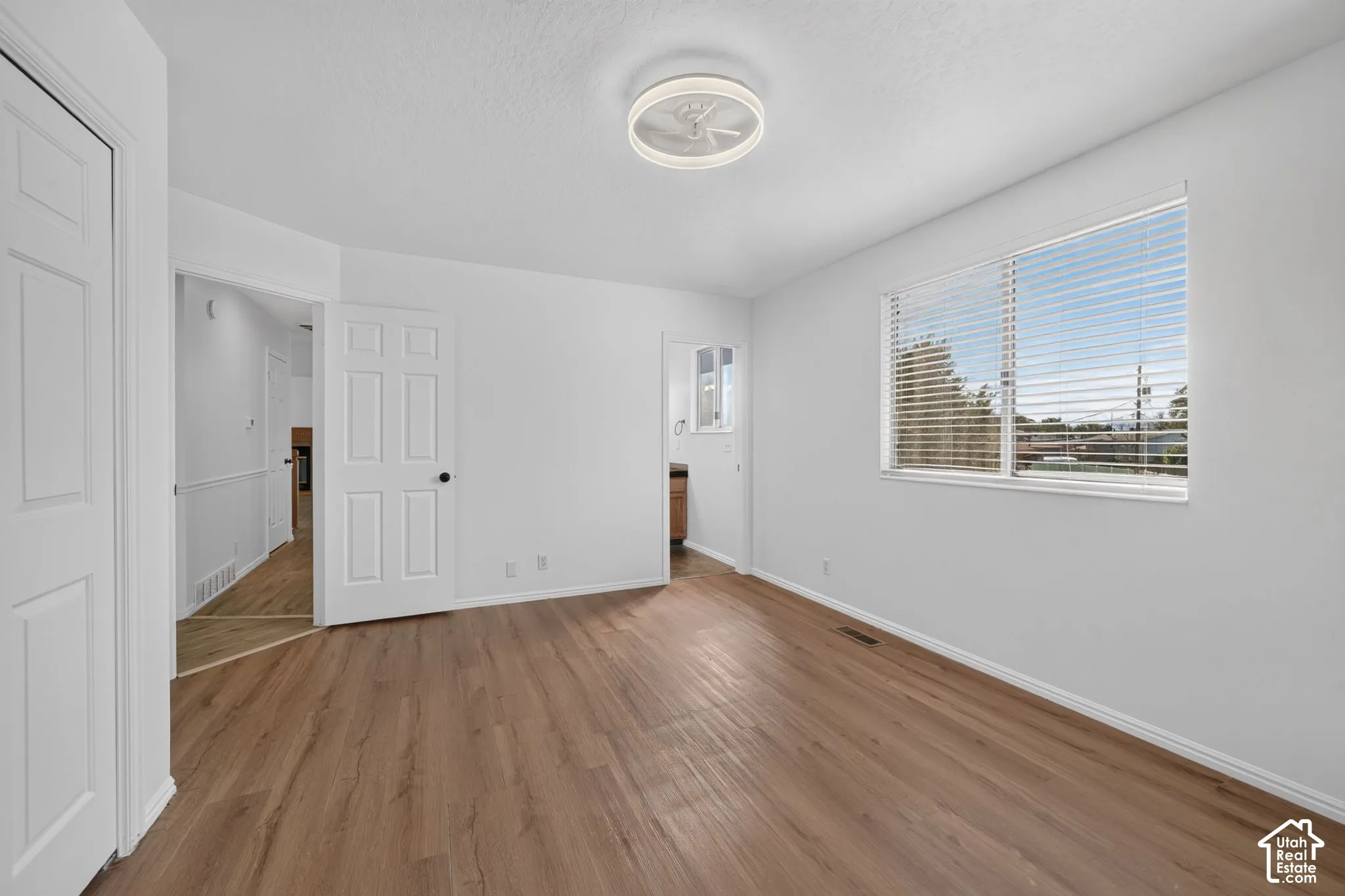Wood-finish flooring, neutral wall tones, multi-panel doors, horizontal window blinds, and a circular ceiling-mounted light fixture