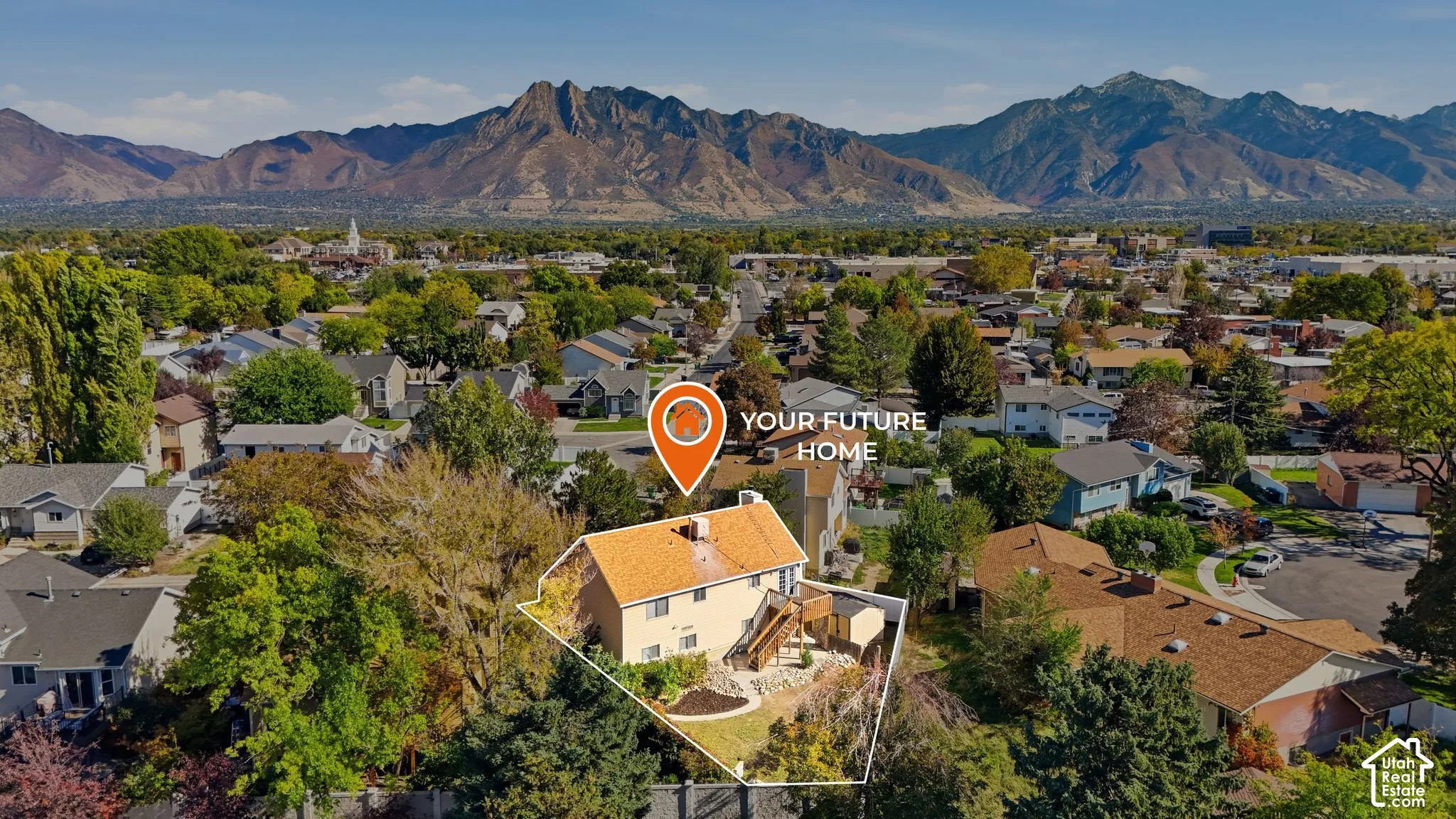 Aerial view of property featuring a multi-level residence with a wood-tone shingle roof, an elevated rear deck, and a landscaped yard, set against a prominent mountain backdrop