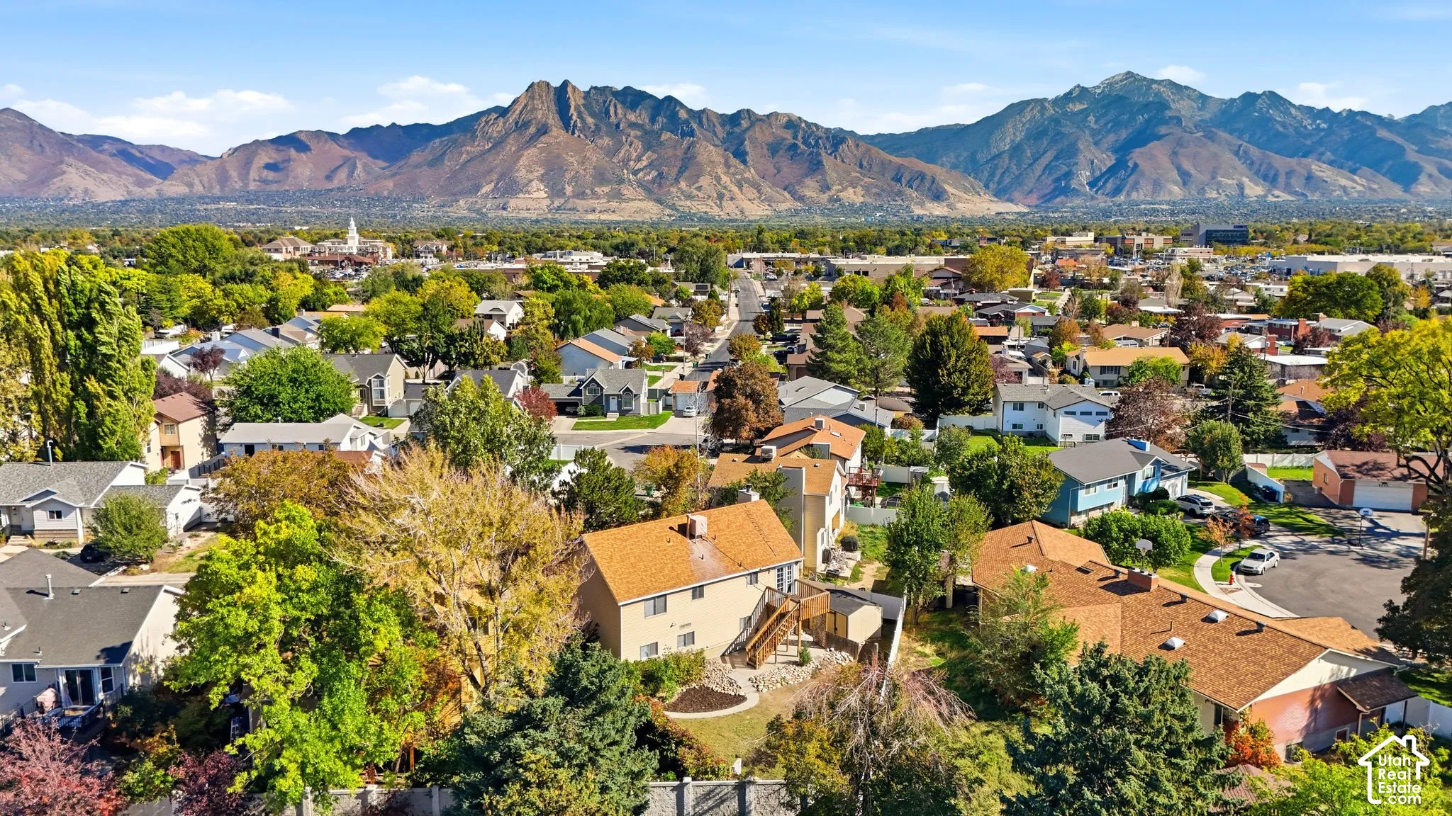 Aerial perspective featuring a multi-level home with a shingled roof, exterior deck, mature landscaping, and an expansive mountain range backdrop