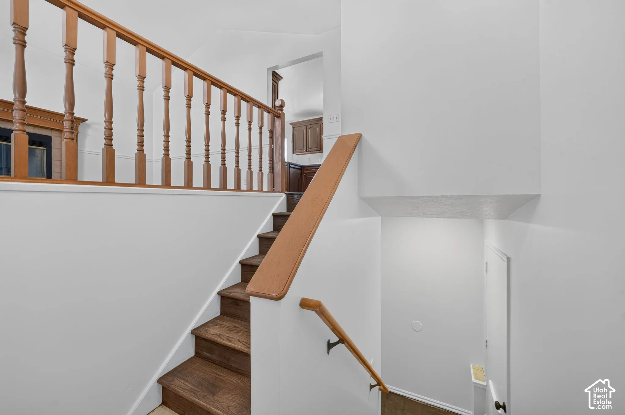Staircase featuring wood-finish treads, a wooden handrail, and a decorative wooden balustrade