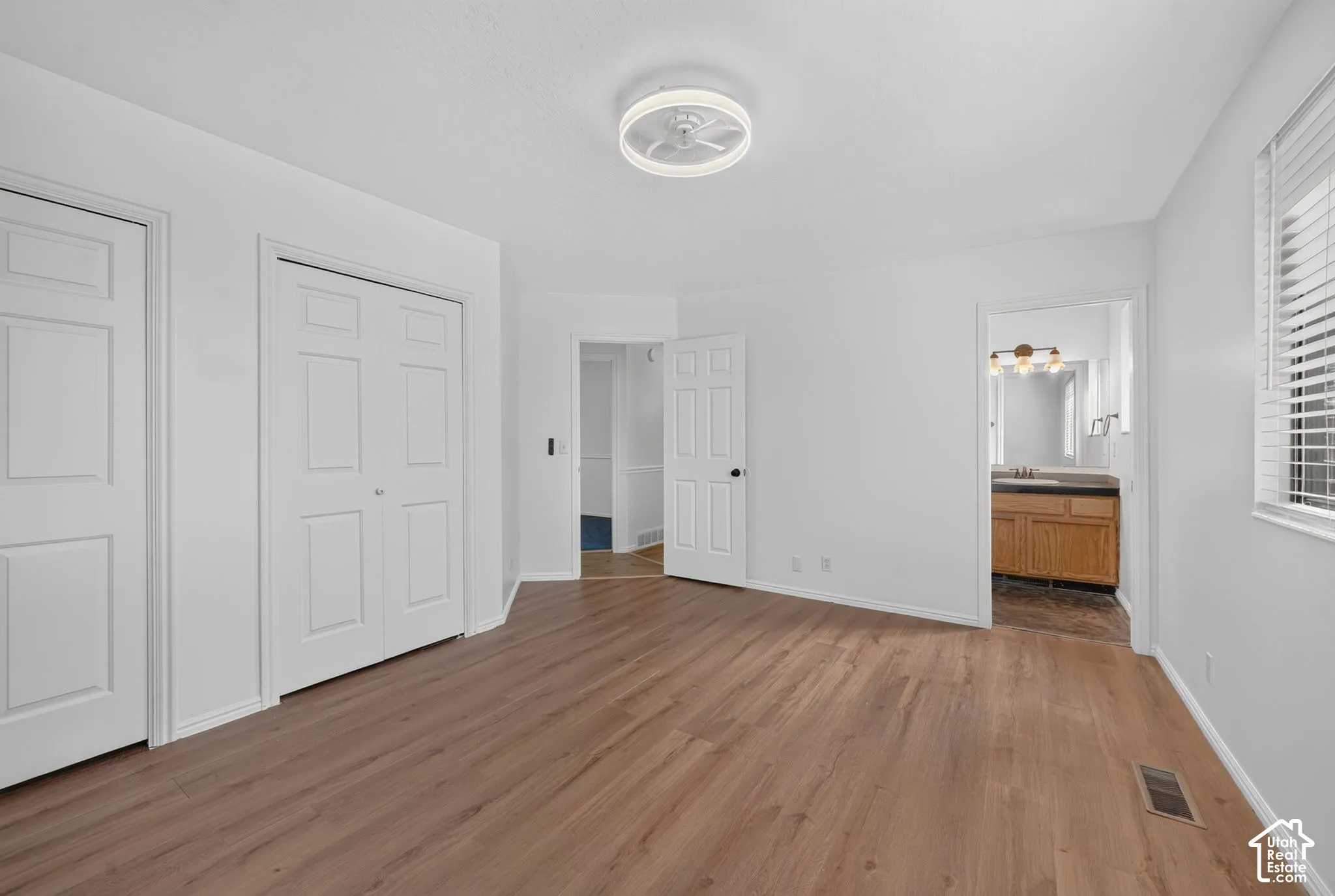 Wood-finish flooring, dual-panel closet doors, flush-mount circular LED ceiling light, and horizontal window blinds