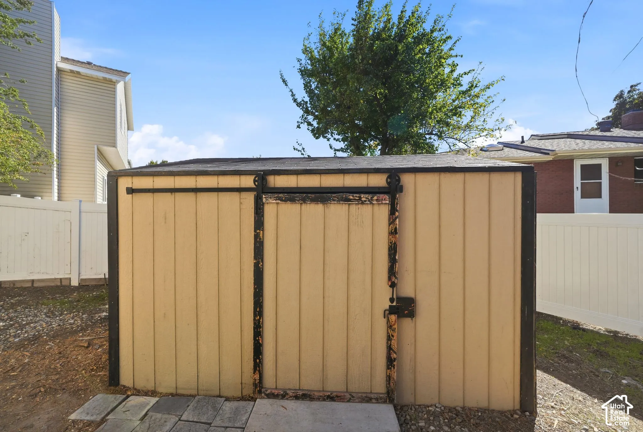 Storage shed featuring vertical wood-panel siding, a black metal sliding door track, and a concrete paver entrance
