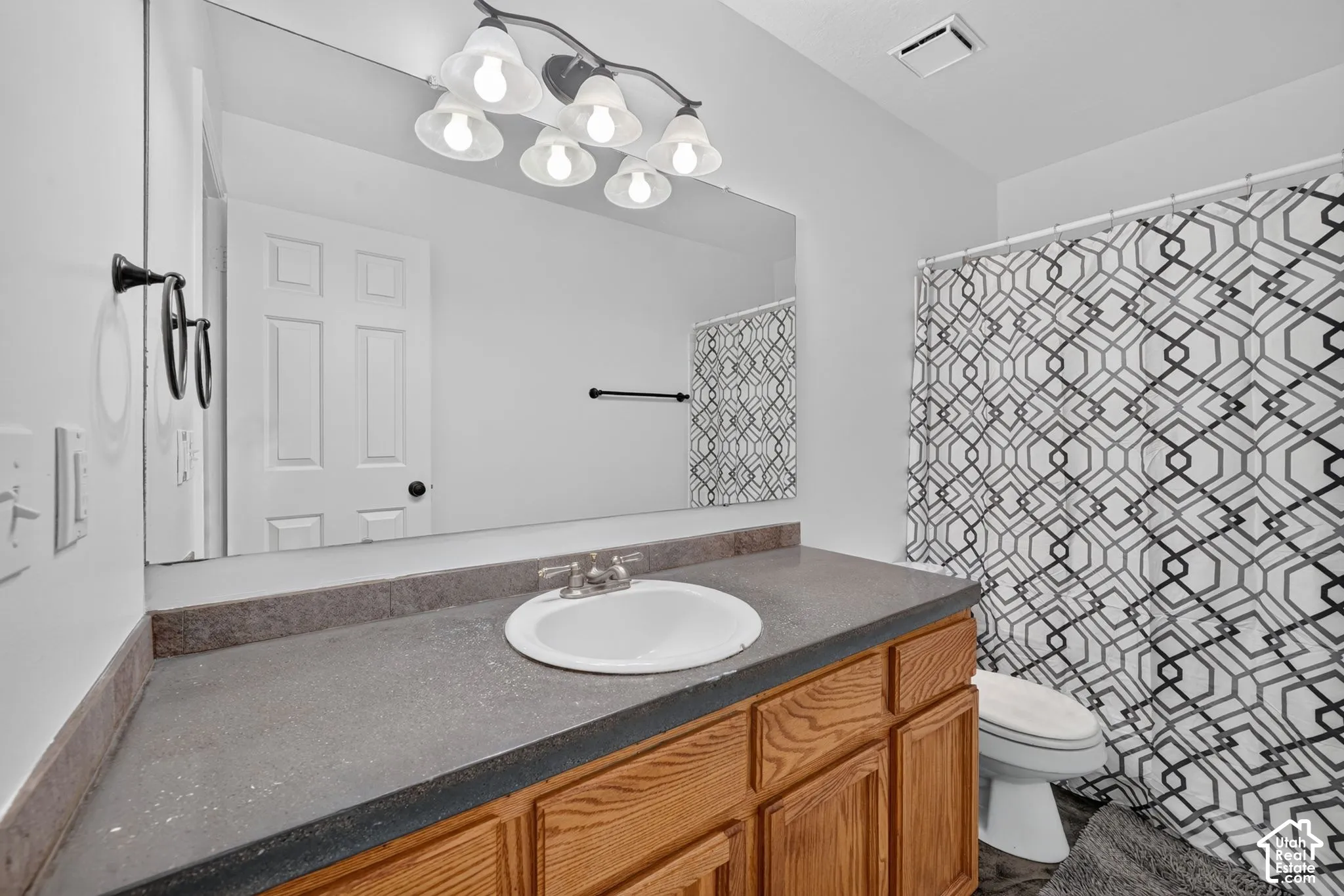 Bathroom featuring a wood-finish vanity with a stone-composite countertop, integrated sink, five-light fixture, and full-width wall mirror