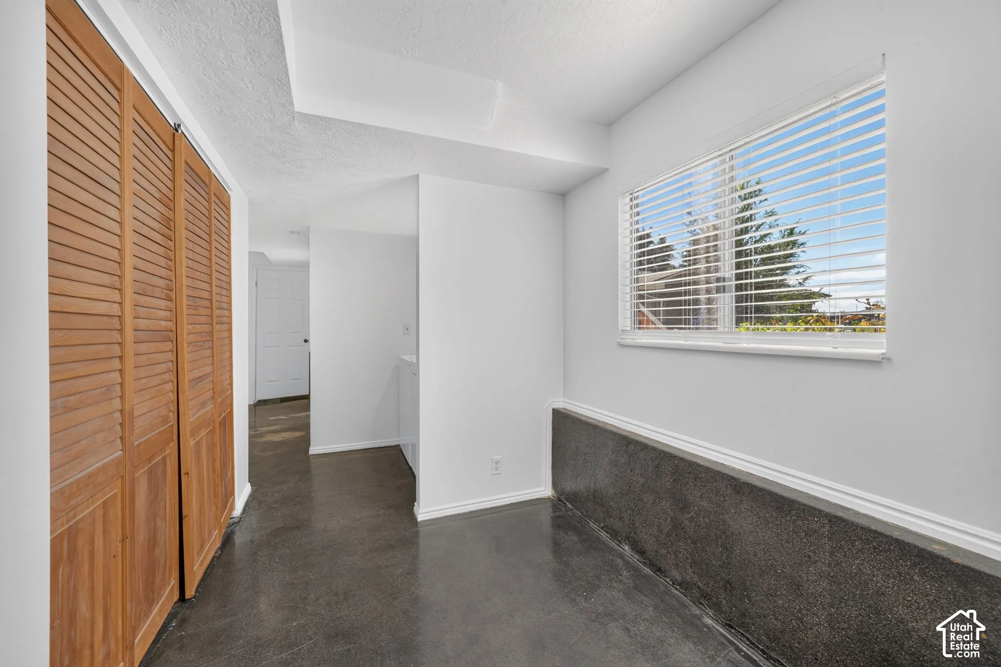 Interior space featuring wood-finish louvered closet doors, polished concrete flooring, and a window with integrated horizontal blinds