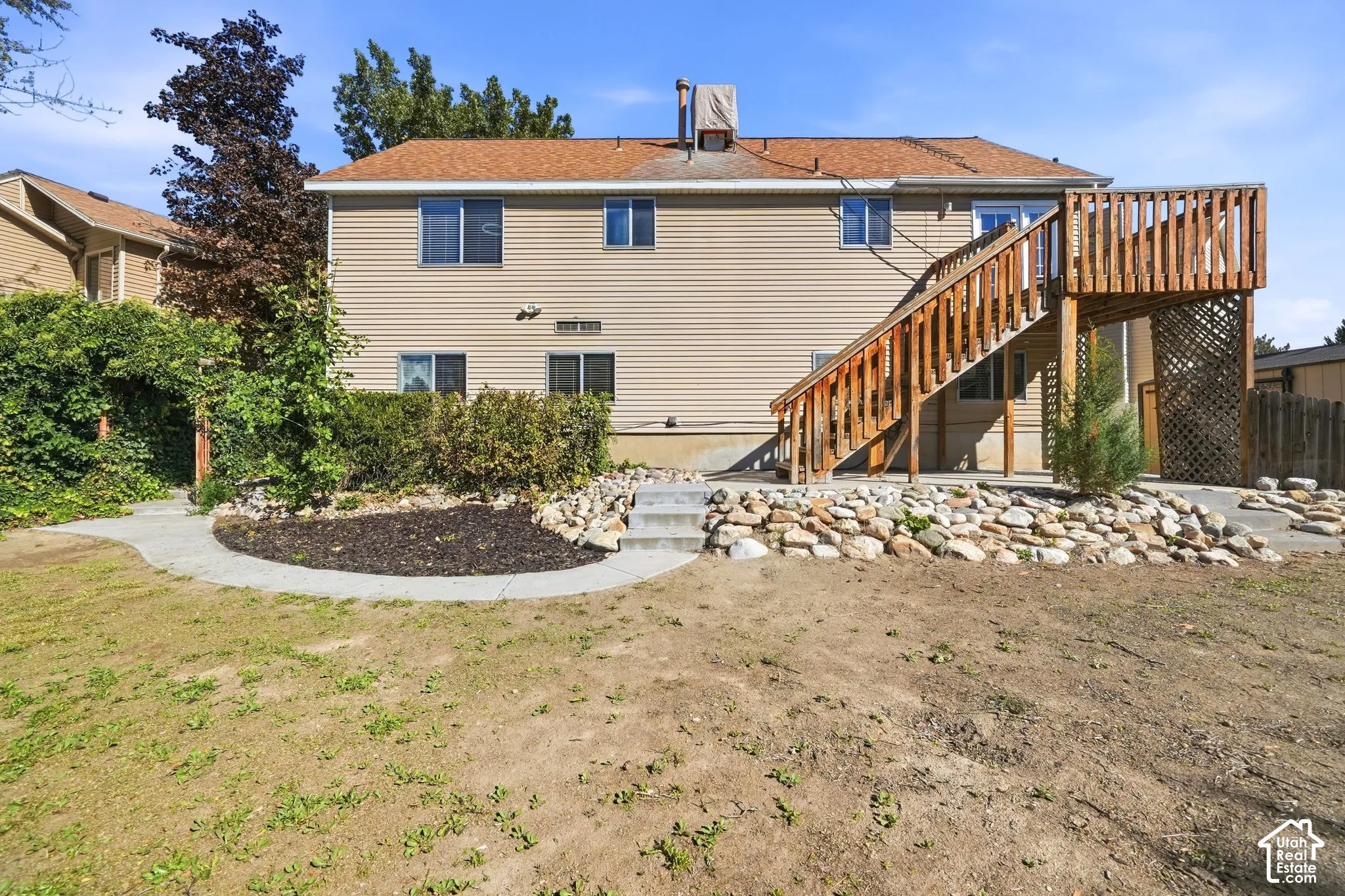 Two-story residence featuring horizontal vinyl siding, a wooden elevated deck with stairs, stone hardscaping, and mature landscaping