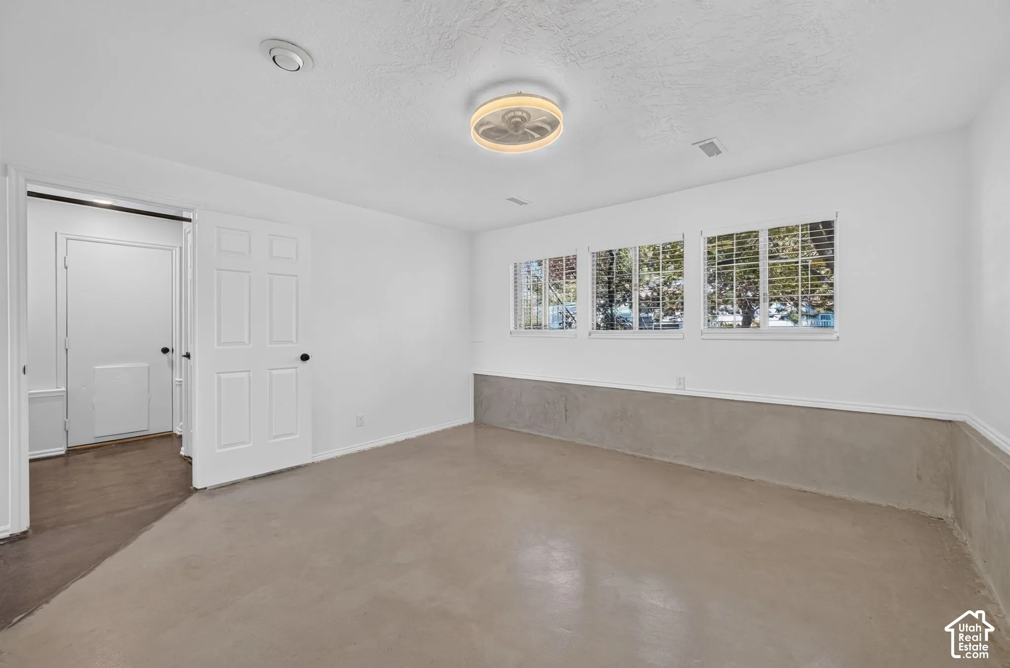 Room featuring painted concrete flooring, a tiered ceiling fan with integrated lighting, triple-pane windows, and white six-panel interior doors