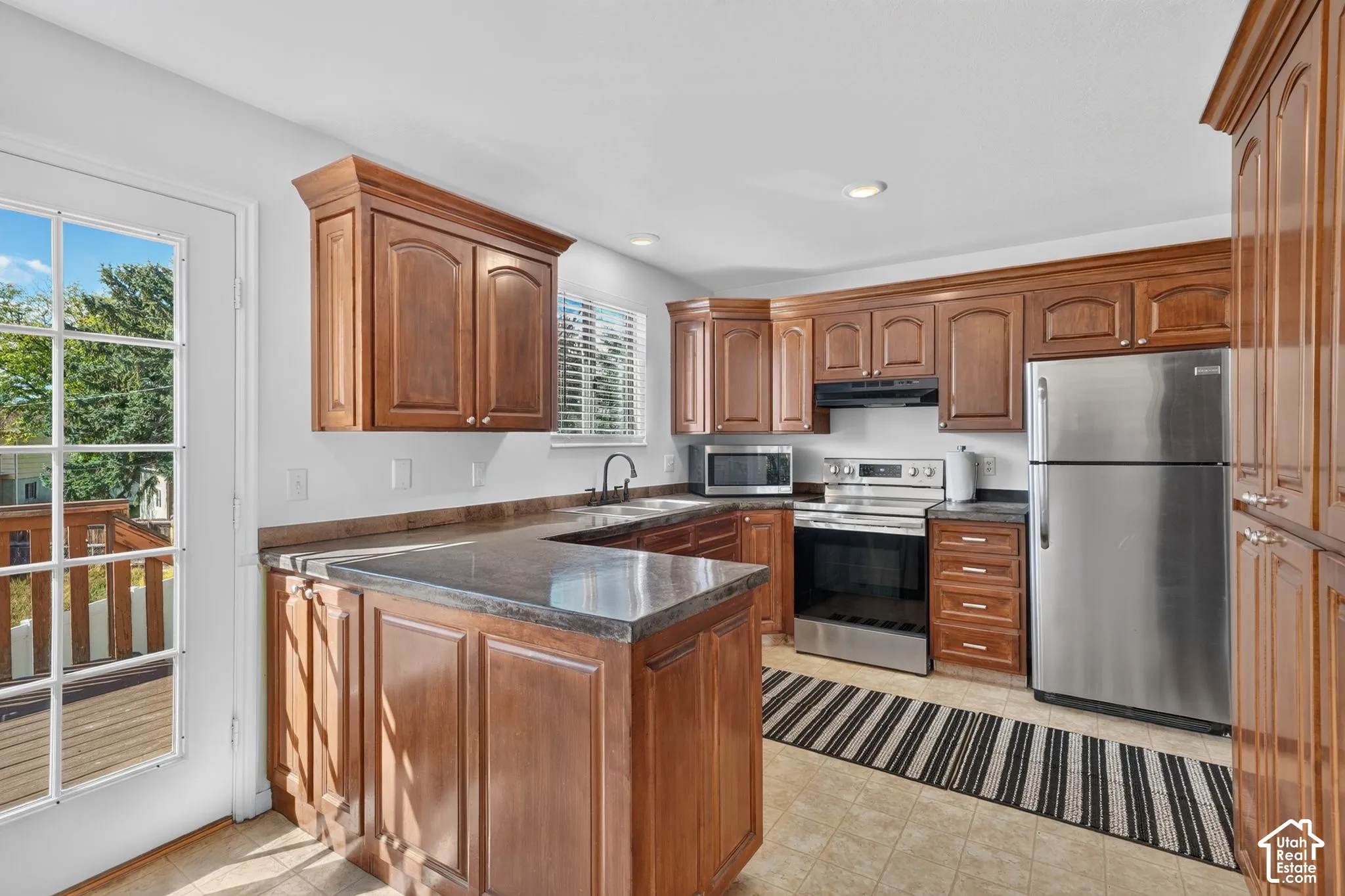 Kitchen featuring wood cabinetry, stone-finish countertops, stainless steel appliances, and a full-light glass door