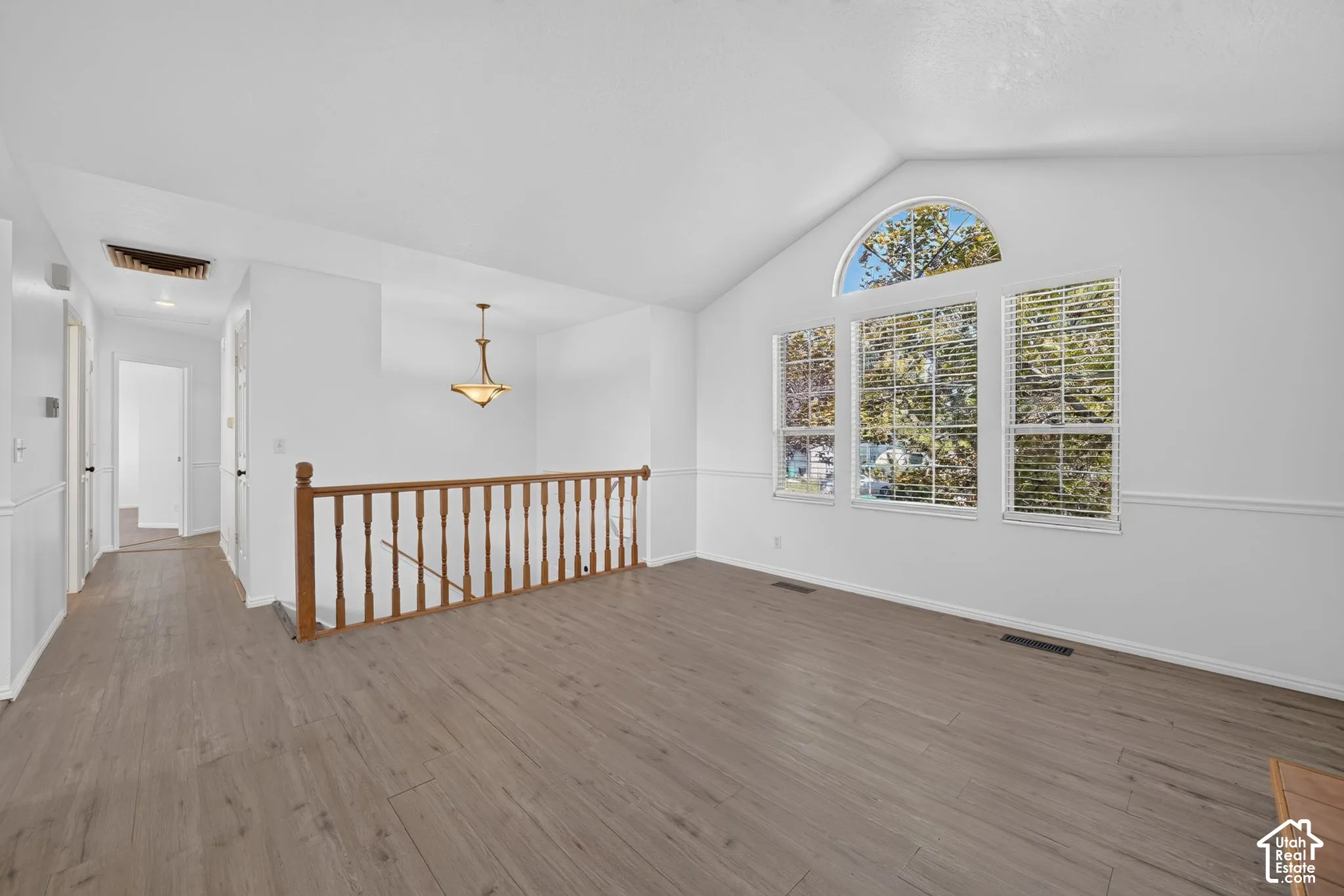 Vaulted ceilings with wood-finish flooring, featuring a classic wooden balustrade, a semi-circular accent window, and an integrated pendant light fixture