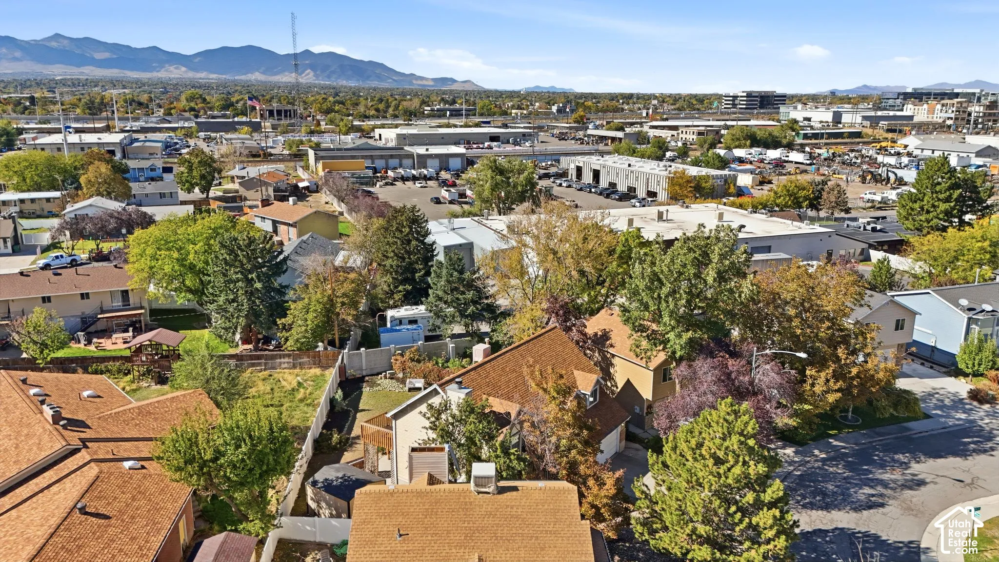 Aerial perspective showcasing a residential lot with mature trees, established landscaping, mountain backdrop, and suburban placement