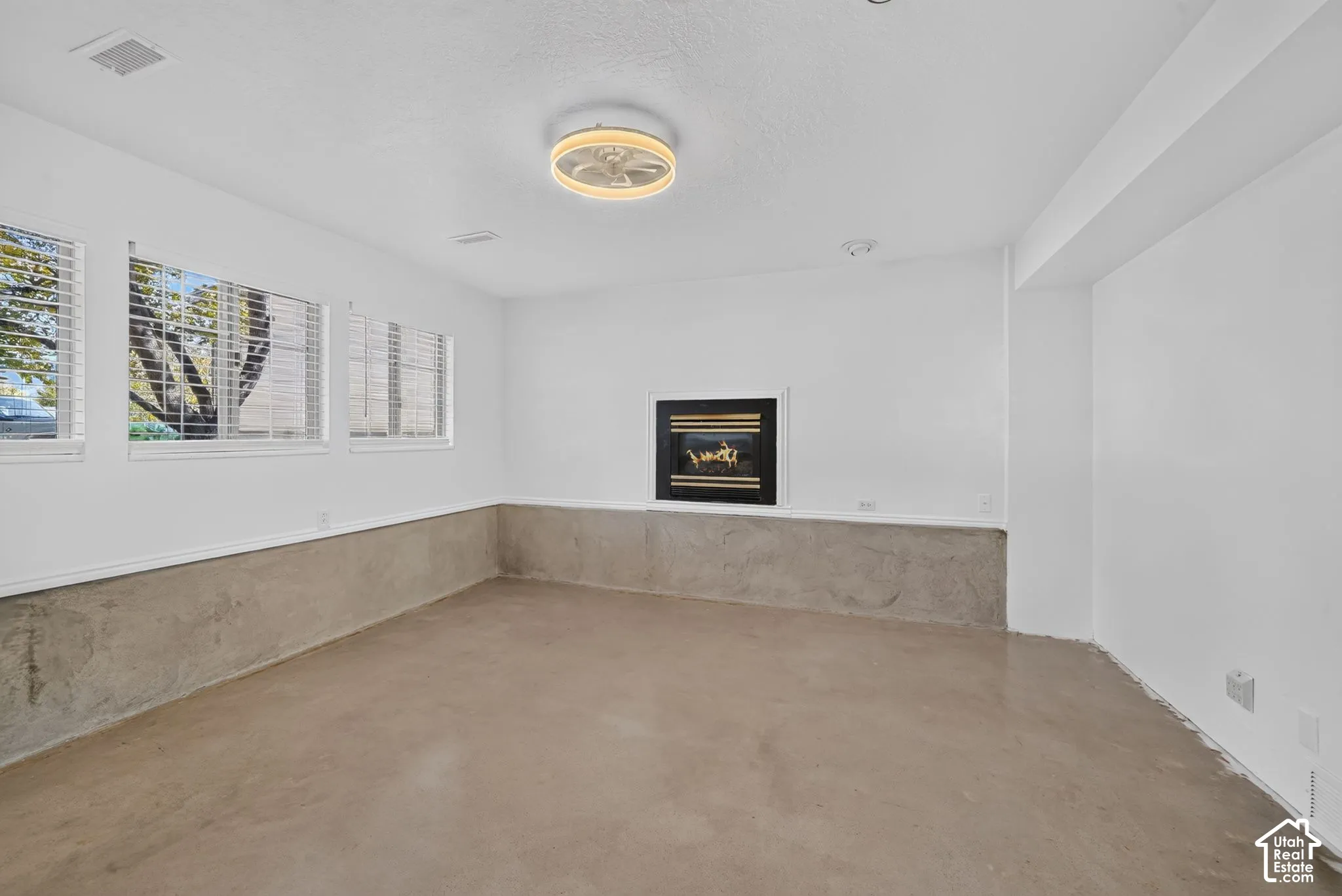 Interior space featuring a built-in wall-mounted fireplace, multi-pane windows, concrete flooring, textured concrete wainscoting, and a circular ceiling fixture