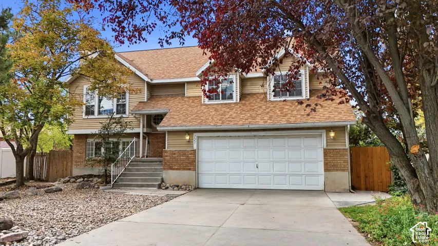 Two-story exterior featuring tan horizontal siding, brick facade accents, a multi-gabled roofline, and an attached two-car garage