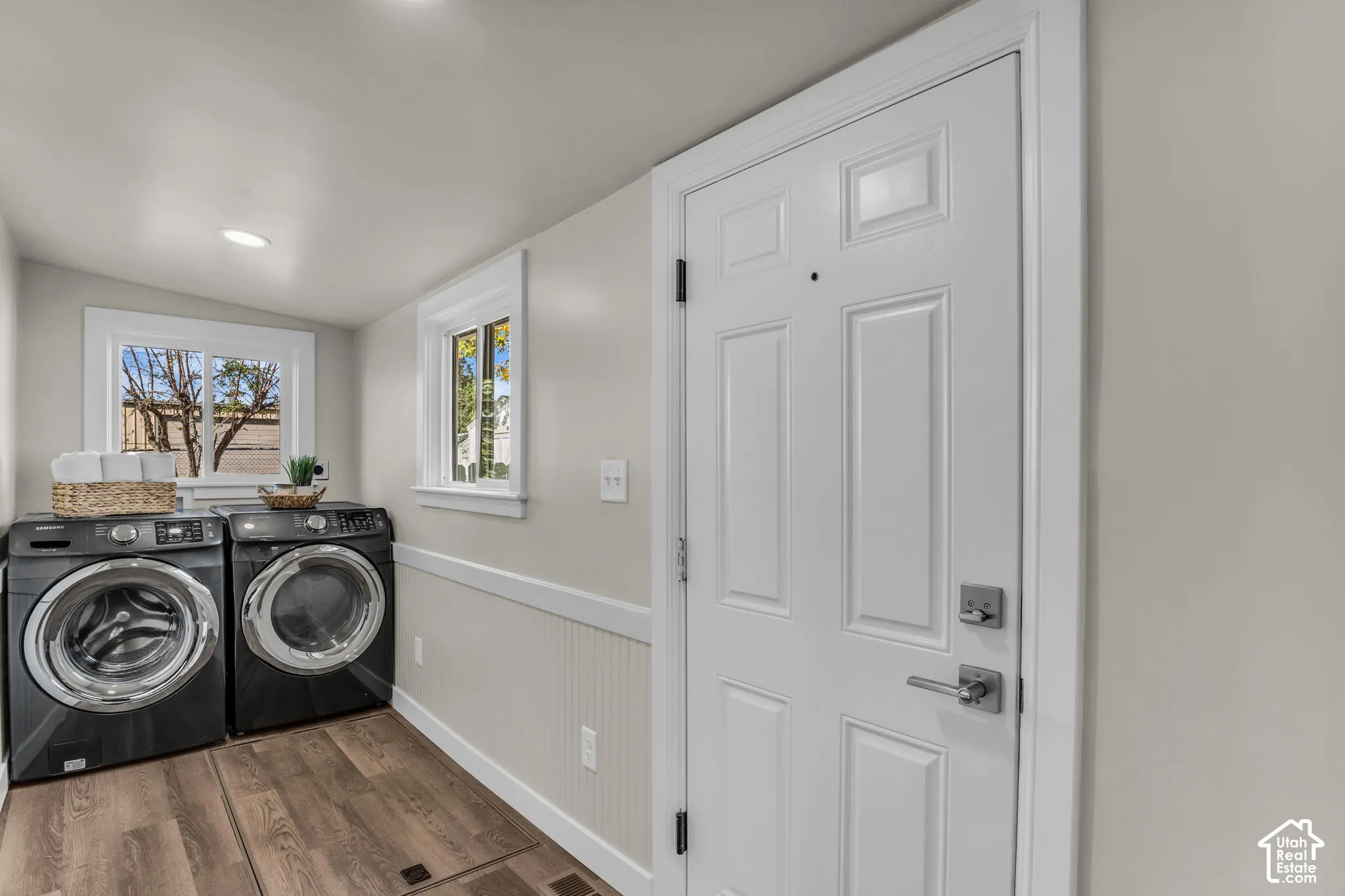 Dedicated laundry area featuring wood-finish flooring, two windows with white trim, recessed lighting, and wainscoting