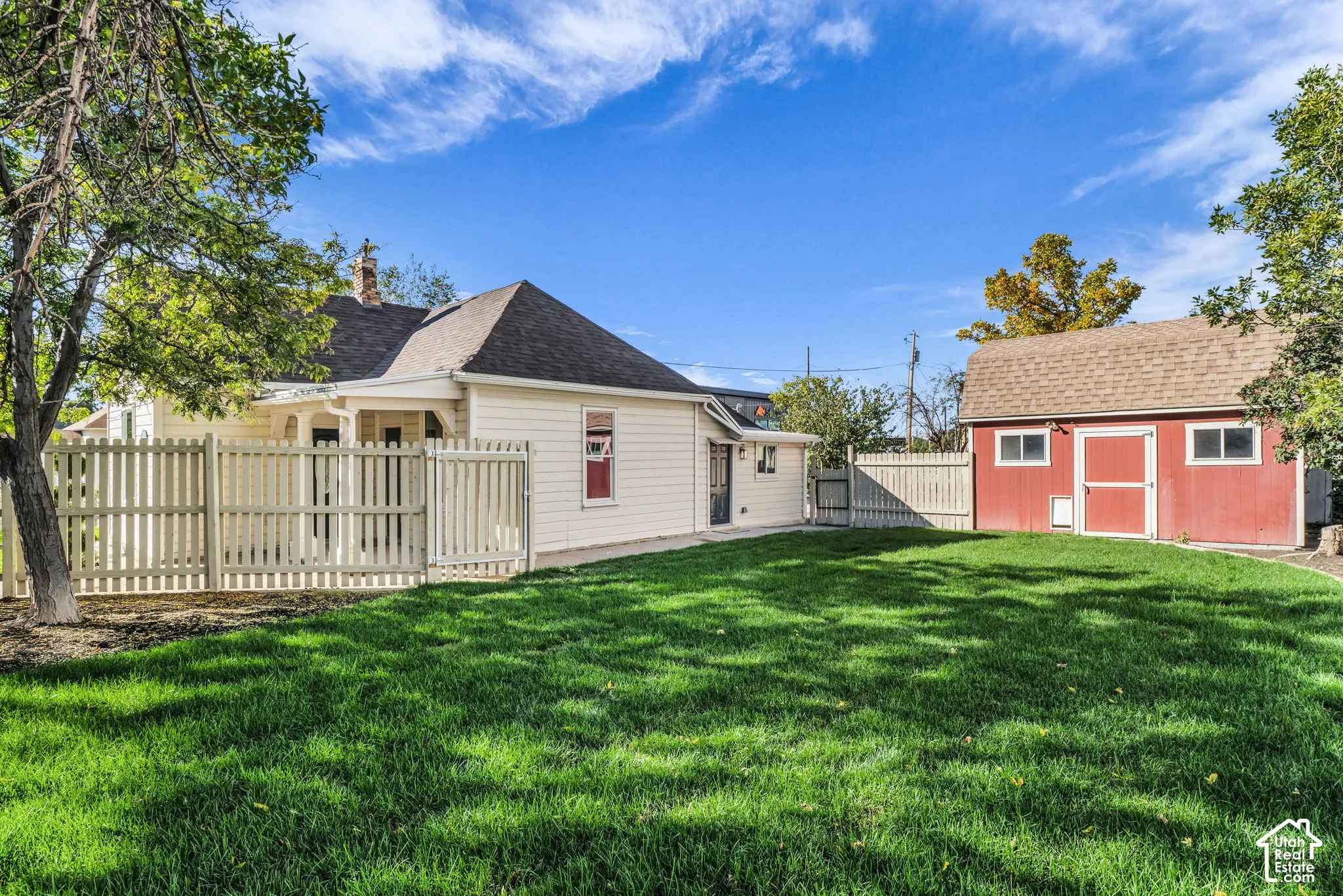 Expansive grassy yard with a white picket fence, mature trees, and a detached red shed