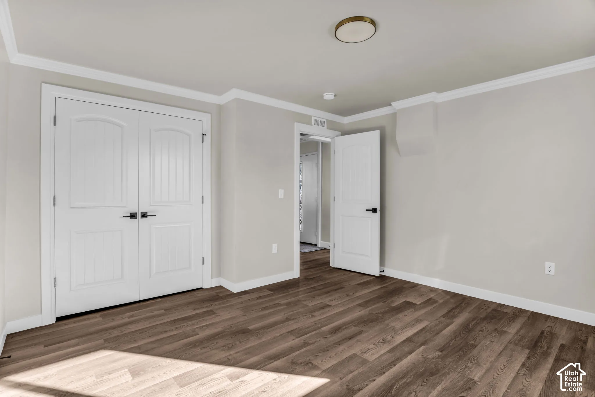 Wood-finish flooring, white double doors with black hardware, crown molding, and a flush mount ceiling light