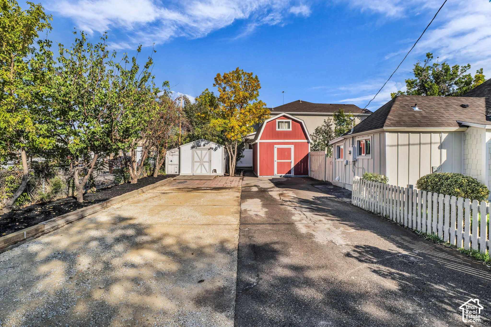 Picket fence, asphalt driveway, gravel driveway, red barn-style shed, white utility shed