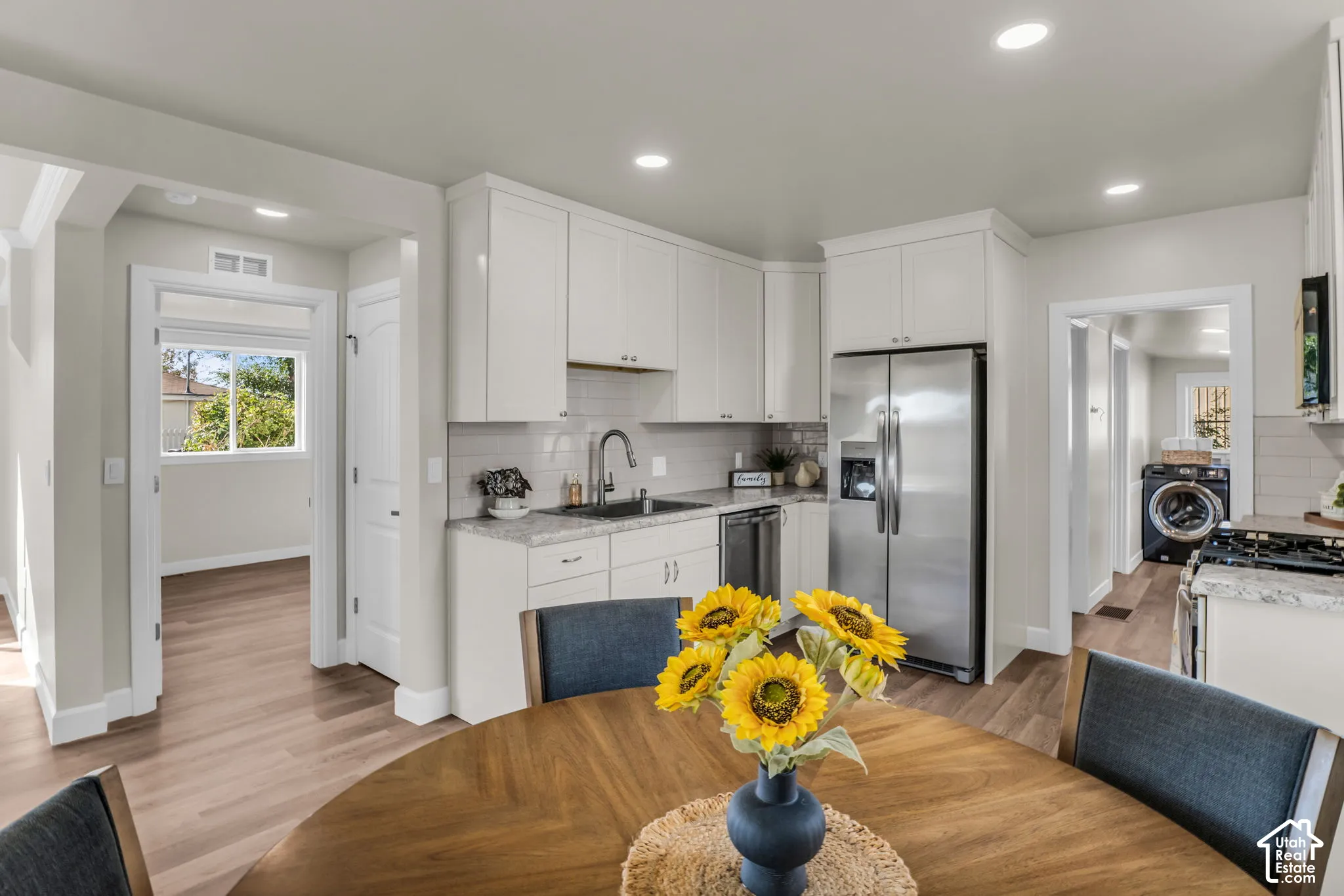 White shaker cabinetry, stainless steel appliances, wood-finish flooring, recessed lighting, and a subway tile backsplash