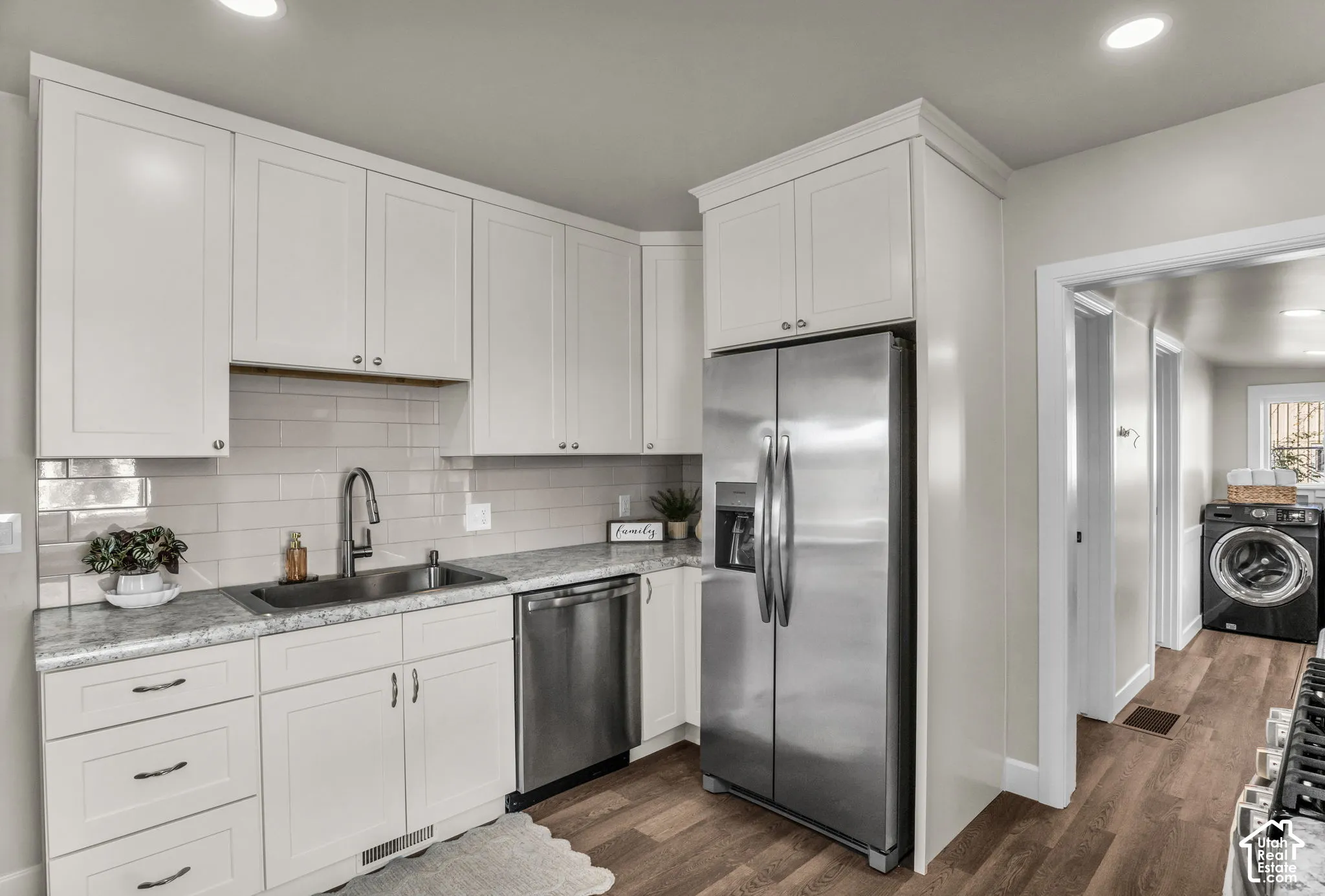 White cabinetry with crown molding, stainless steel appliances, light-toned countertop, subway tile backsplash, and wood-finish flooring