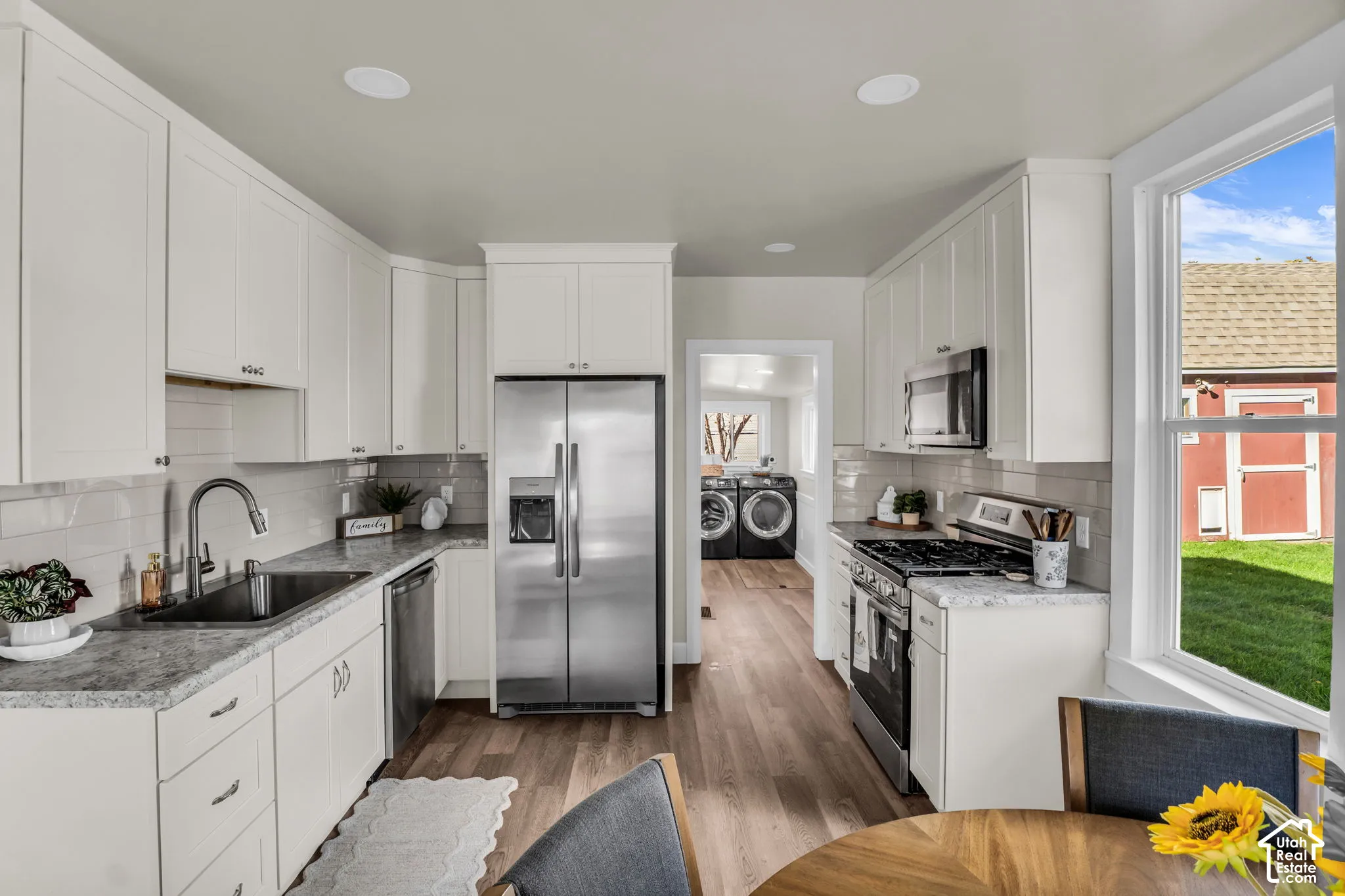 Kitchen featuring white cabinetry, light-toned countertops, stainless steel appliances, and wood-finish flooring