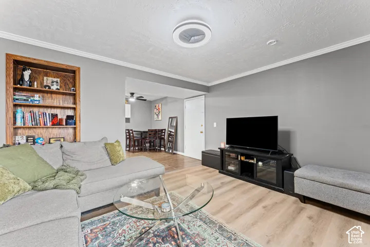 Living area featuring wood-finish flooring, built-in wooden shelving, and crown molding