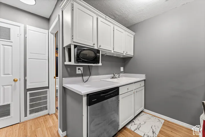 White cabinetry with upper and lower storage, stainless steel dishwasher, white countertop with integrated sink, and wood-finish flooring