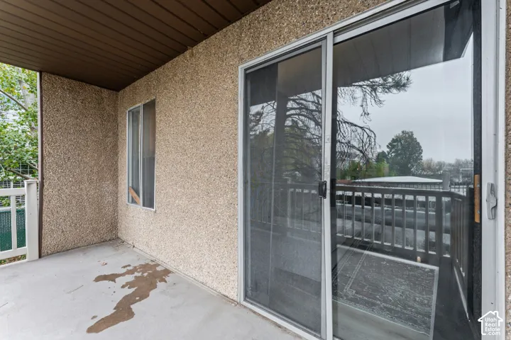 Covered patio featuring concrete flooring, textured stone-finish exterior siding, and a sliding glass door with integrated screen