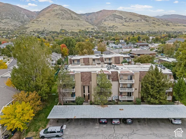 Multi-story complex featuring private balconies, masonry exterior cladding, and covered carport parking, set against a backdrop of mountain scenery