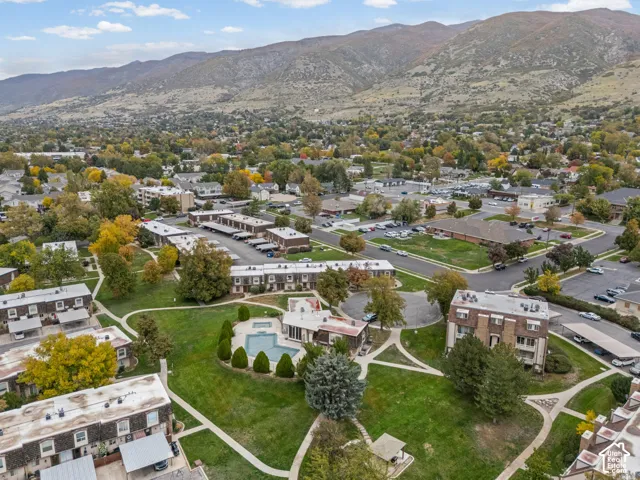 Aerial perspective featuring a swimming pool, expansive common grounds, concrete pathways, and a backdrop of mountain terrain