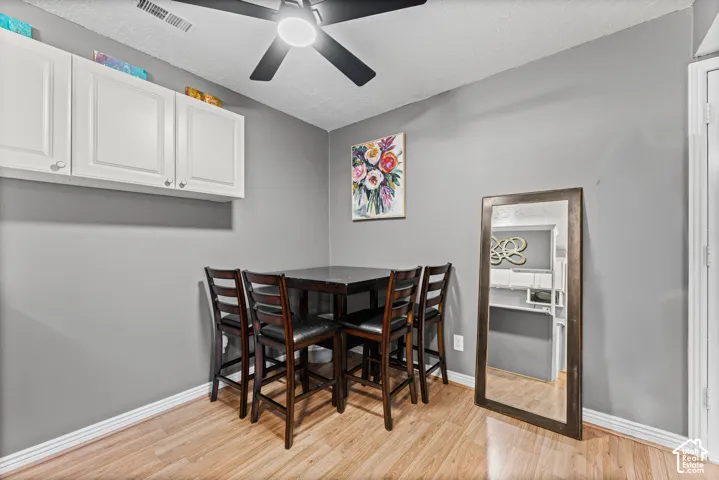 Wood-finish flooring, white shaker-style wall-mounted cabinetry, and a ceiling-mounted light fixture with matte black blades