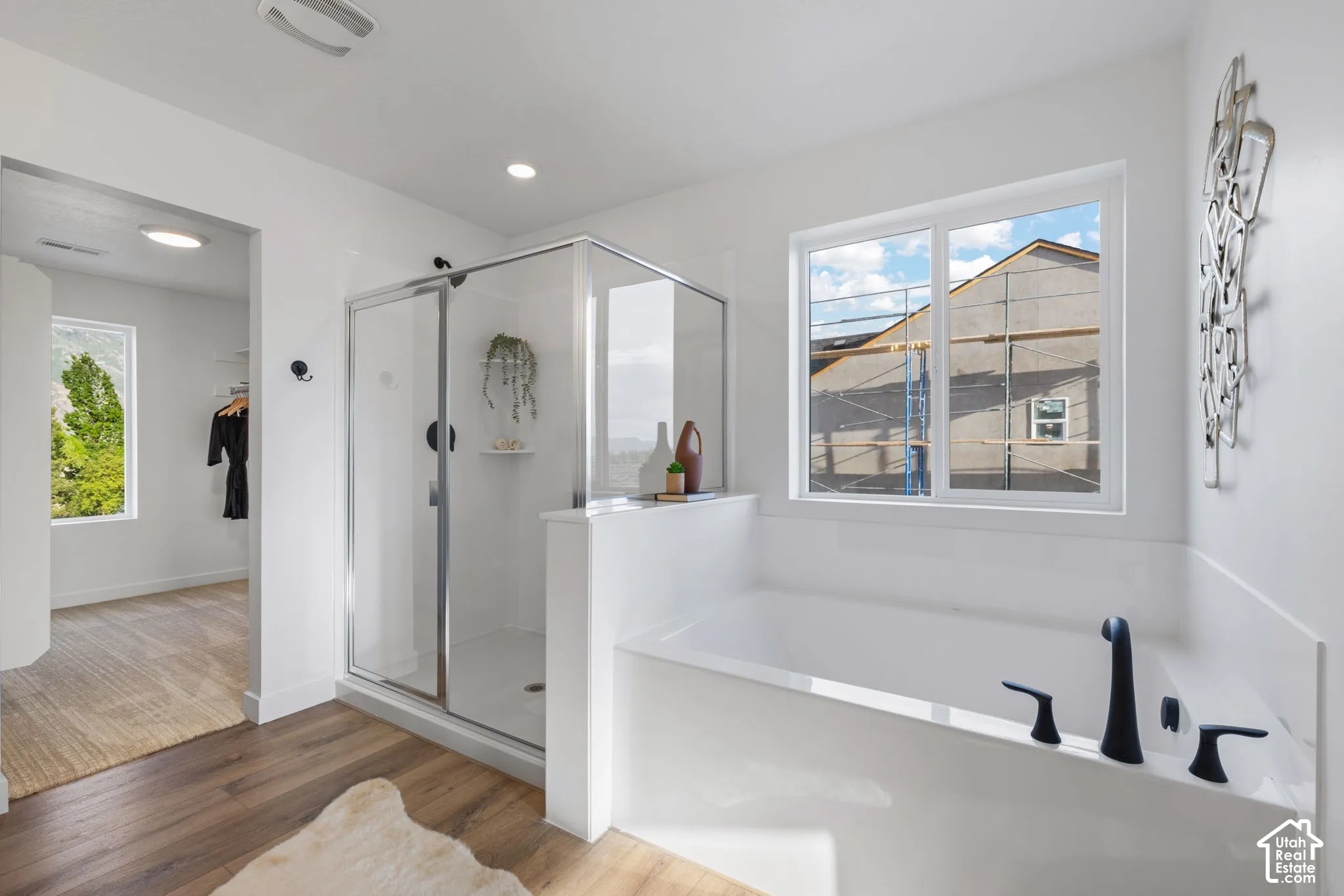Bathroom featuring wood-finish flooring, a glass-enclosed shower with matte black fixtures, and a soaking tub with a wall-mounted matte black faucet