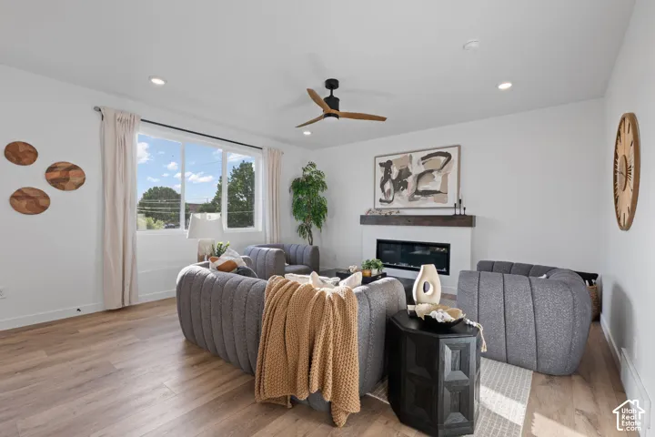 Living area featuring wood-finish flooring, a wall-mounted electric fireplace with a wood mantel, recessed lighting, and a multi-blade ceiling fan