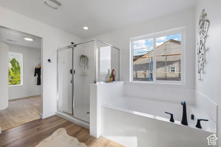 Bathroom featuring wood-finish flooring, a glass-enclosed shower with matte black fixtures, and a soaking tub with a wall-mounted matte black faucet