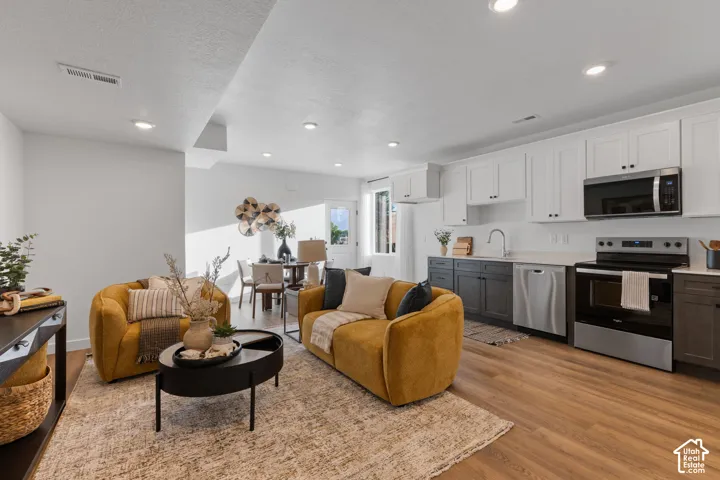 Kitchen featuring white upper cabinetry, dark lower cabinetry, stainless steel appliances, wood-finish flooring, and recessed lighting