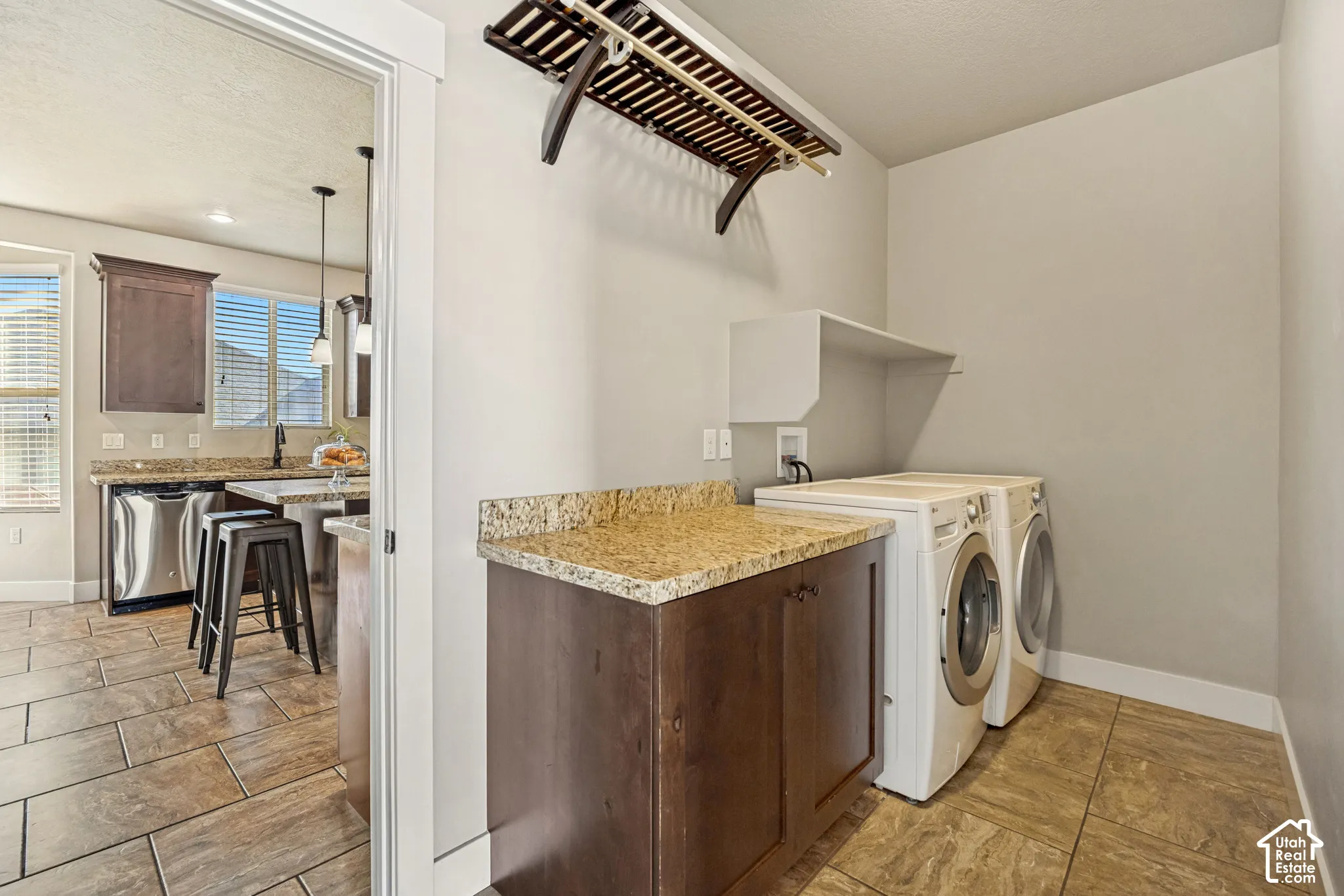 Laundry area featuring stone-surface countertops, custom wood cabinetry, tile flooring, and wall-mounted overhead shelving