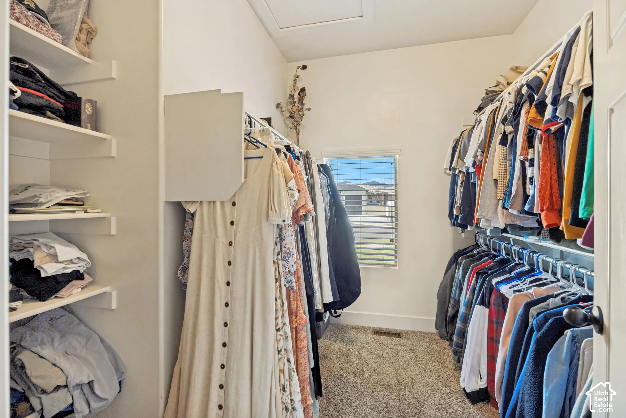 Walk-in closet featuring tiered built-in shelving, dual-level garment hanging rods, and a window with horizontal blinds