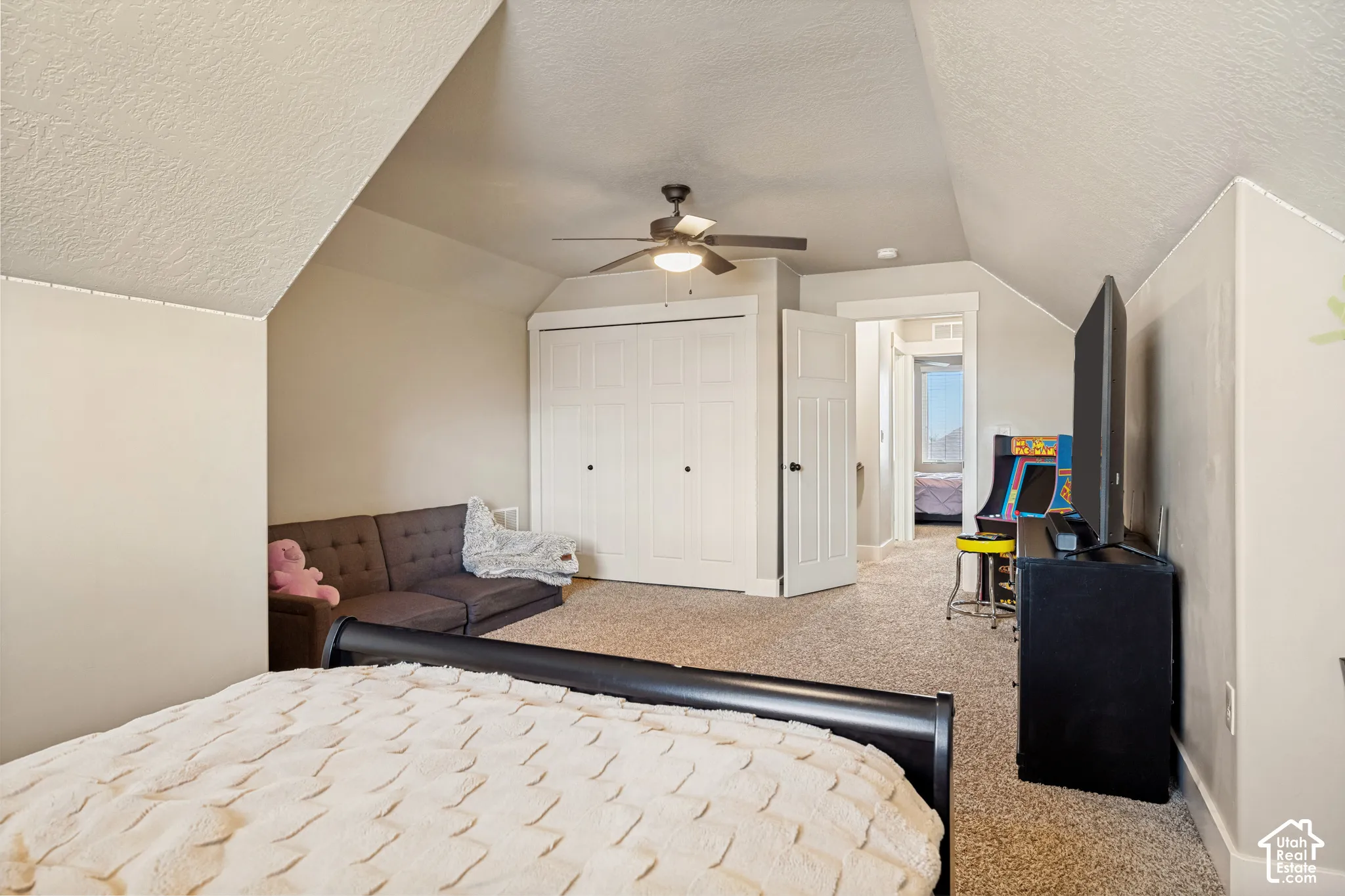 Vaulted ceiling featuring a ceiling fan with integrated lighting, wall-to-wall carpeting, and a dual-panel closet door
